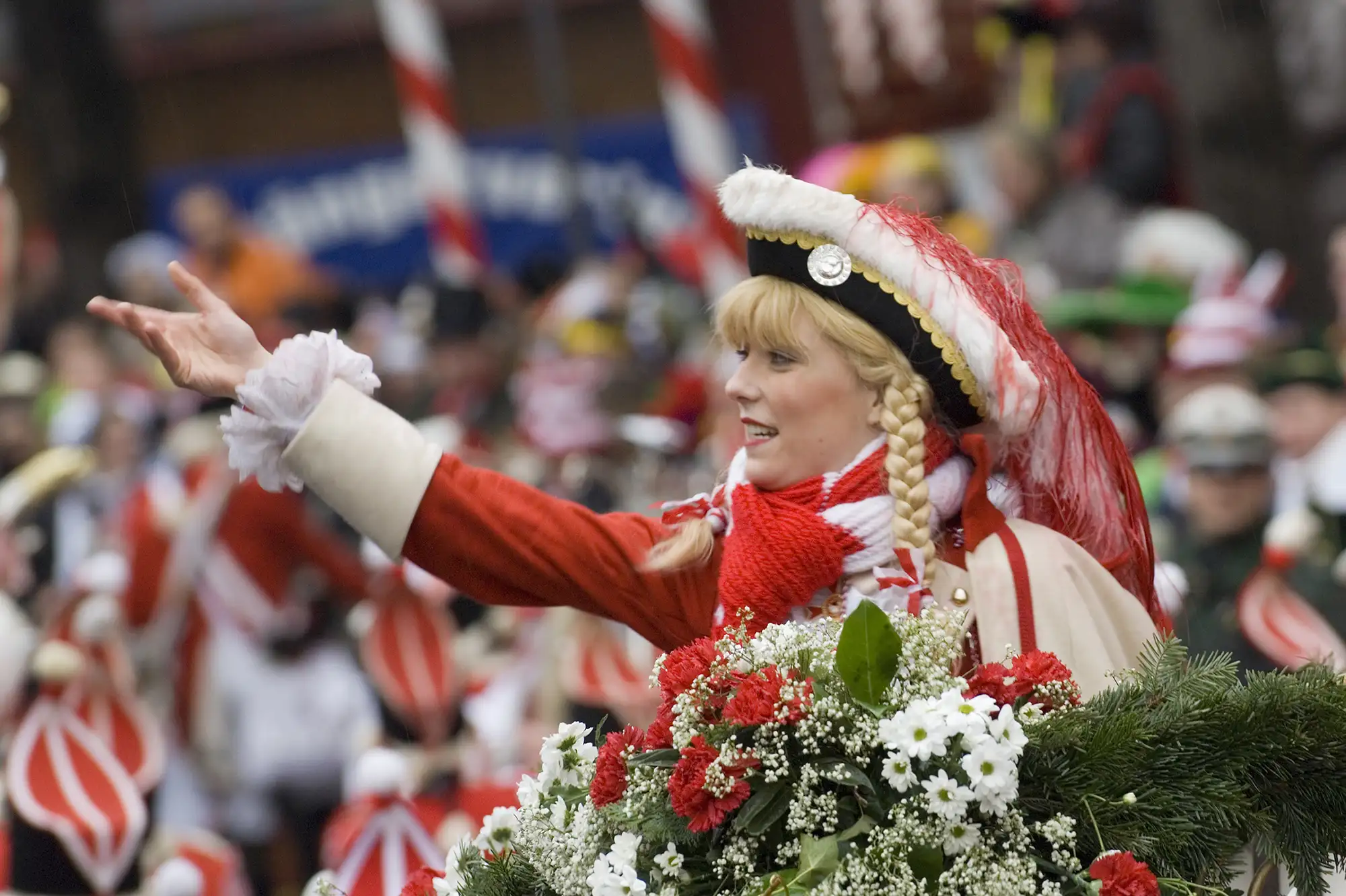 Karneval Köln verkleidete Frau beim Umzug in einem rot weißen Kostüm mit Blumenstrauß und blonder Perücke