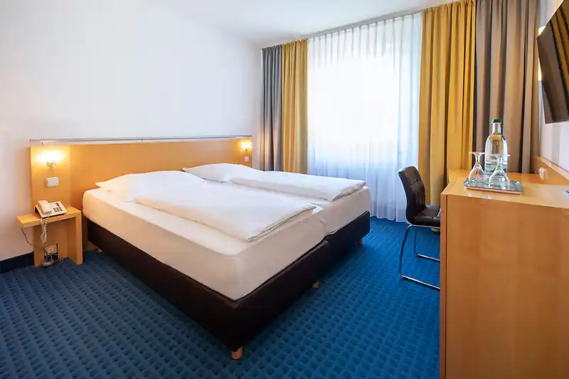Komfortables Doppelzimmer im ACHAT Hotel Suhl mit großem Bett, Schreibtisch, Stuhl, Telefon und Fenster mit Vorhängen