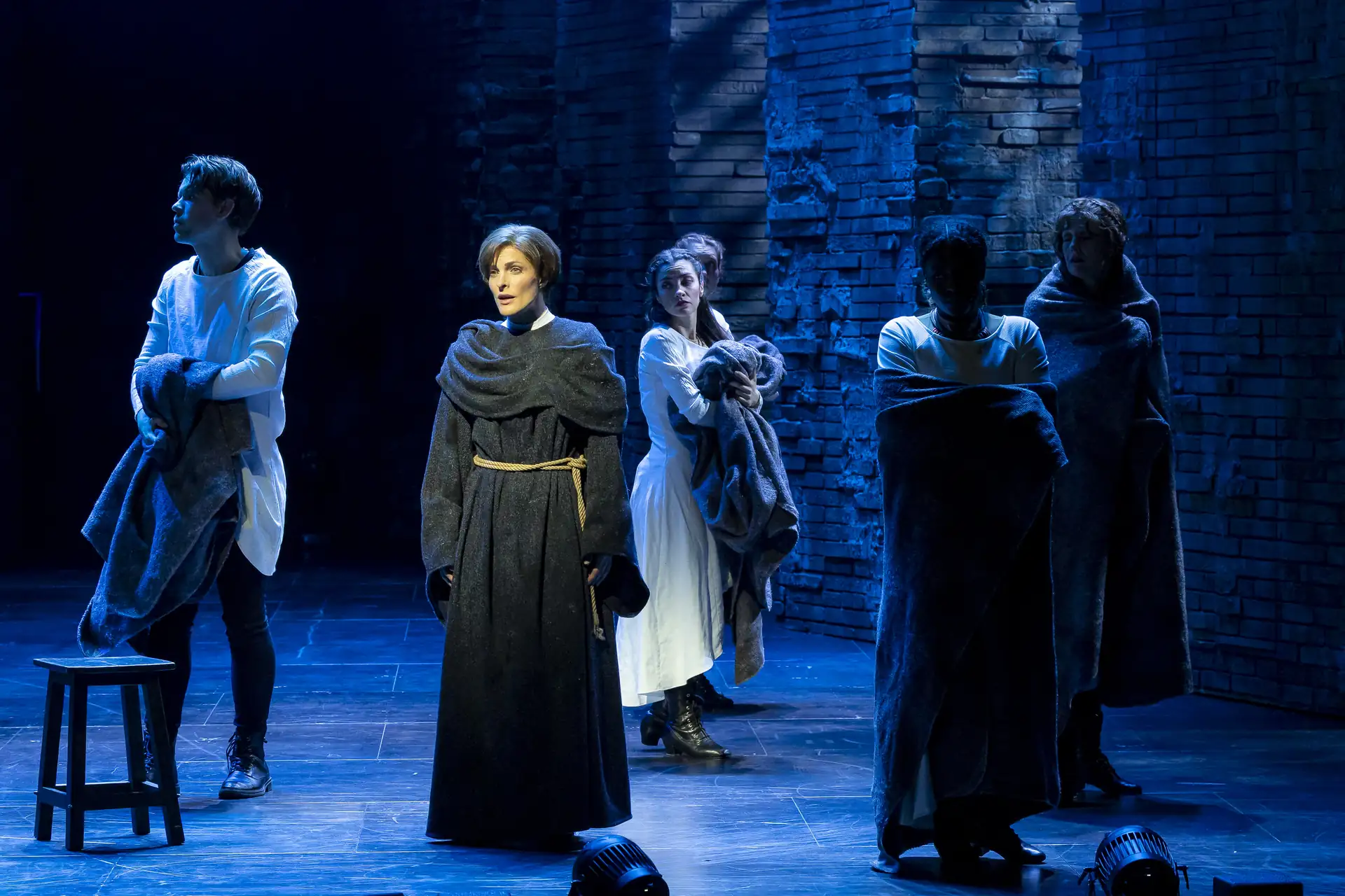 Die Päpstin – Das Musical: Fünf Personen in mittelalterlicher Kleidung stehen auf einer Bühne mit steiniger Kulisse, zwei halten Decken oder Mäntel.