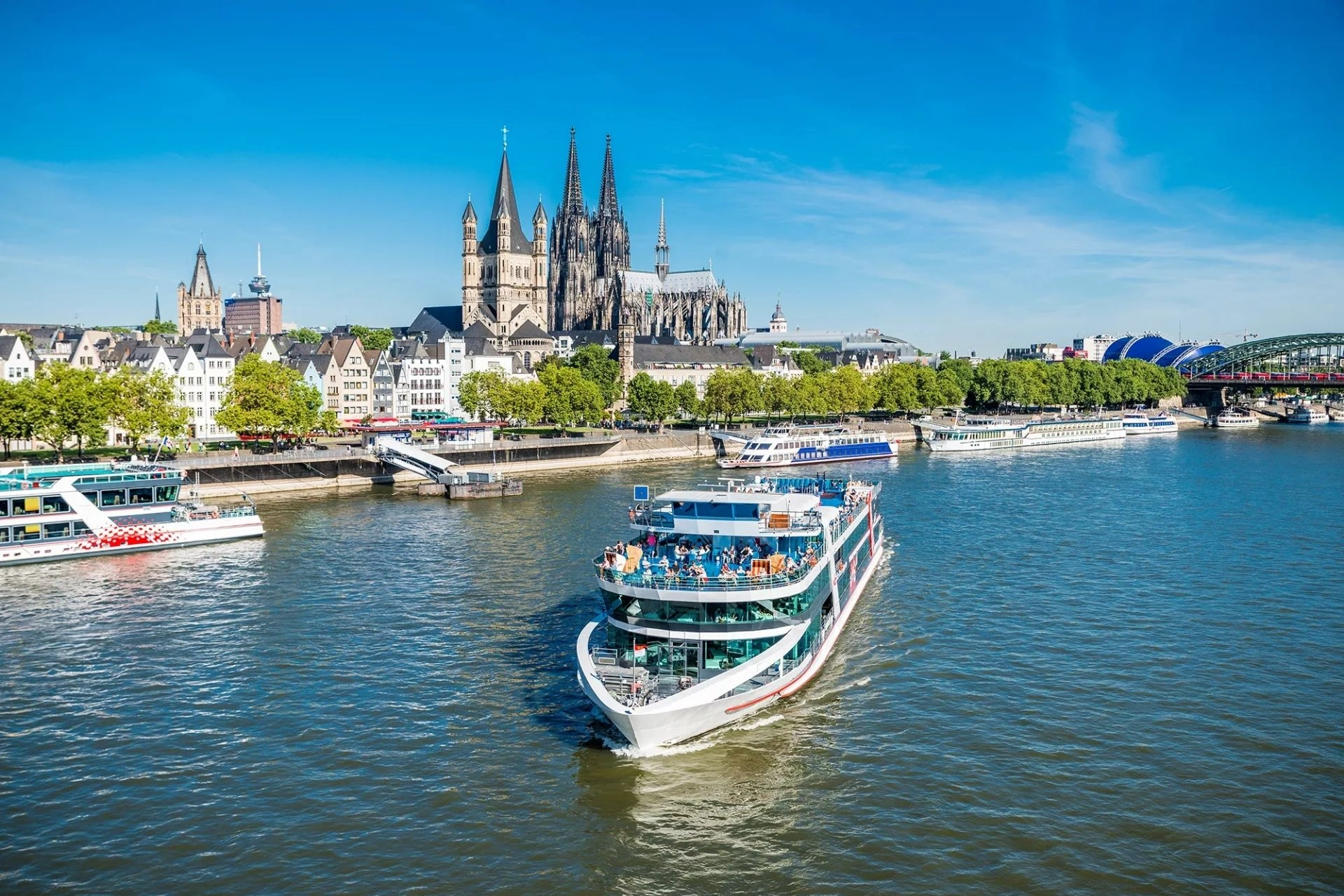 Blick auf den Dom von Köln und die romanische Kirche Groß St. Martin mit einem Ausflugsschiff auf dem Rhein im Vordergrund