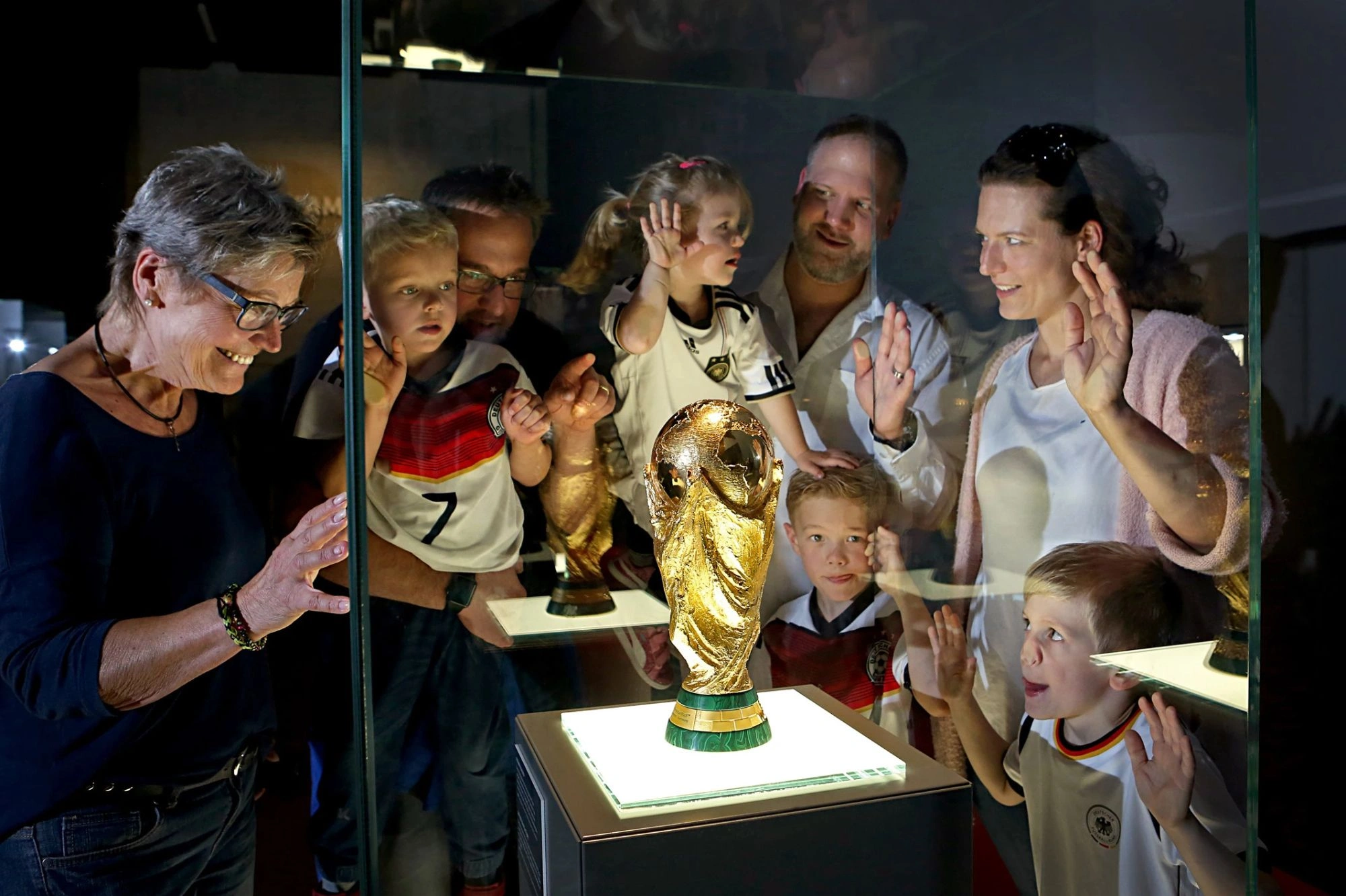 Begeisterte Familie bewundert den Pokal der Weltmeisterschaft im Deutschen Fußballmuseum Dortmund in der Schatzkammer