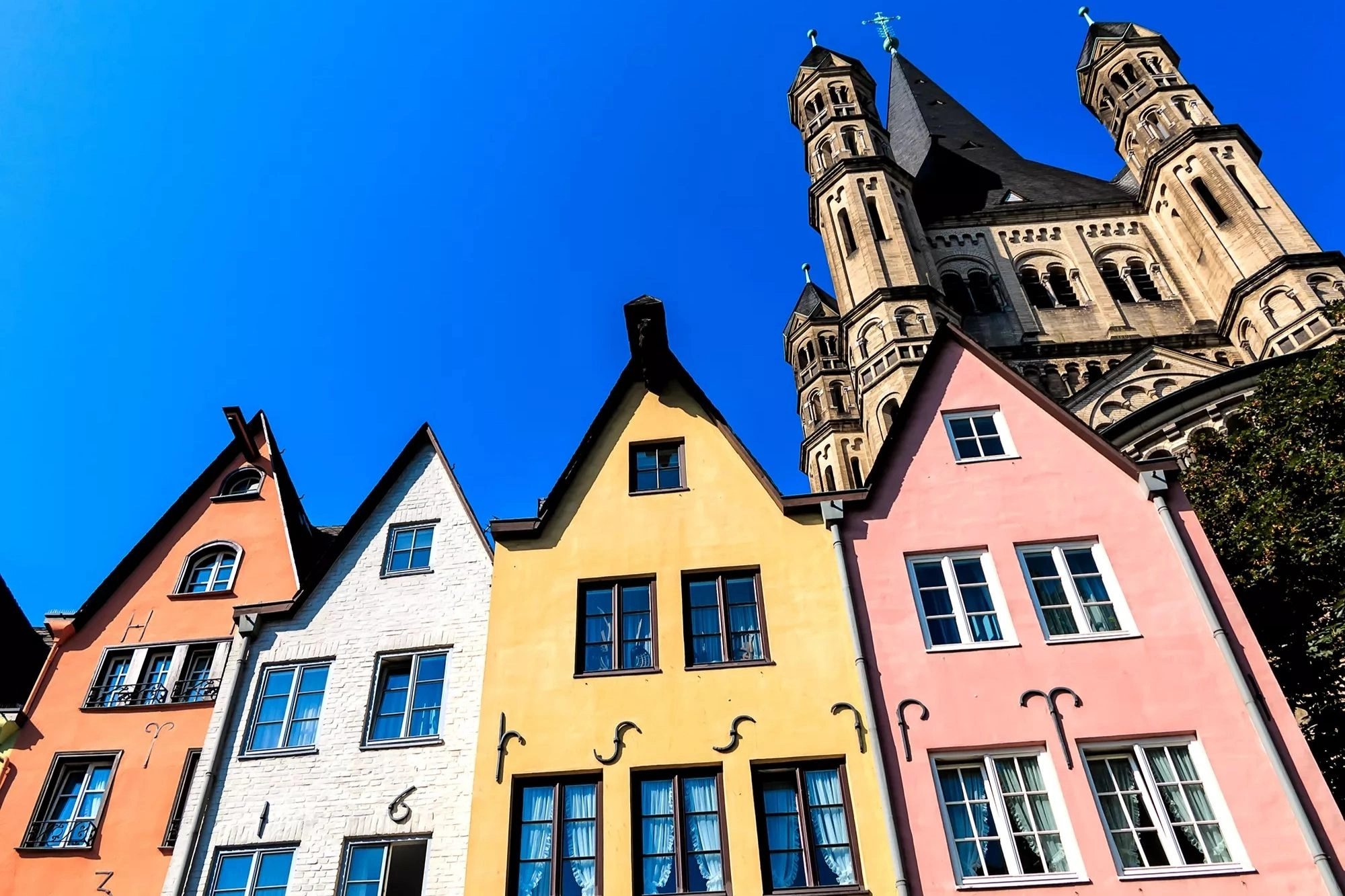 vier bunte Häuser am alten Fischmarkt in der Altstadt von Köln mit der Klosterkirche Groß Sankt Martin im Hintergrund
