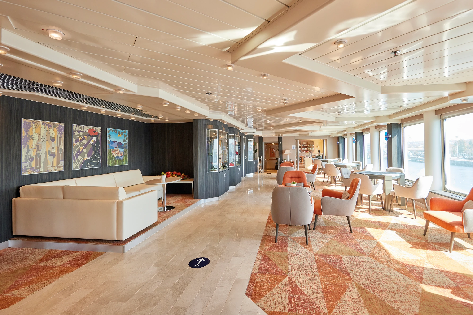 Moderne Lounge auf einem Kreuzfahrtschiff mit großen Fenstern und stilvollem Design.