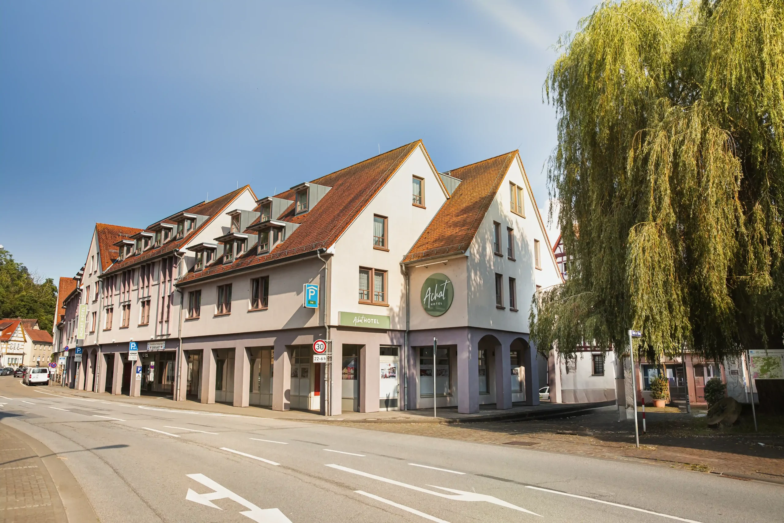 Außenansicht vom Hotel Heppenheim mit rotem Ziegeldach und Arkadengang an der Straßenseite neben einem großen Baum