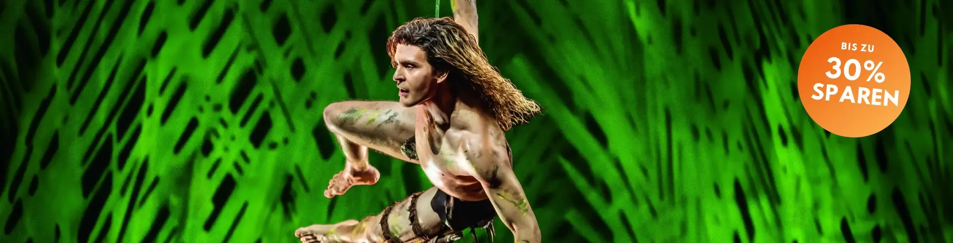 Tarzan in dynamischer Sprungpose vor grünem Hintergrund mit orangefarbenem Kreis und Text 'BIS ZU 30% SPAREN'