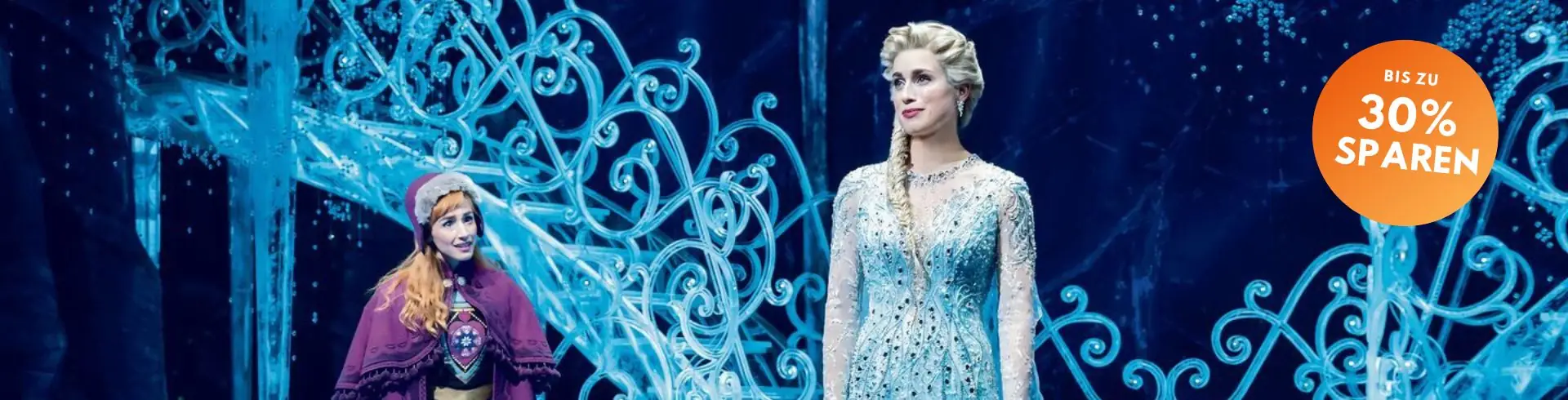 Zwei Frauen in Kostümen vor einem eisblauen, kunstvoll geschwungenen Geländer, rechts eine in einem glitzernden, hellen Kleid, links eine in einem Umhang mit Kapuze