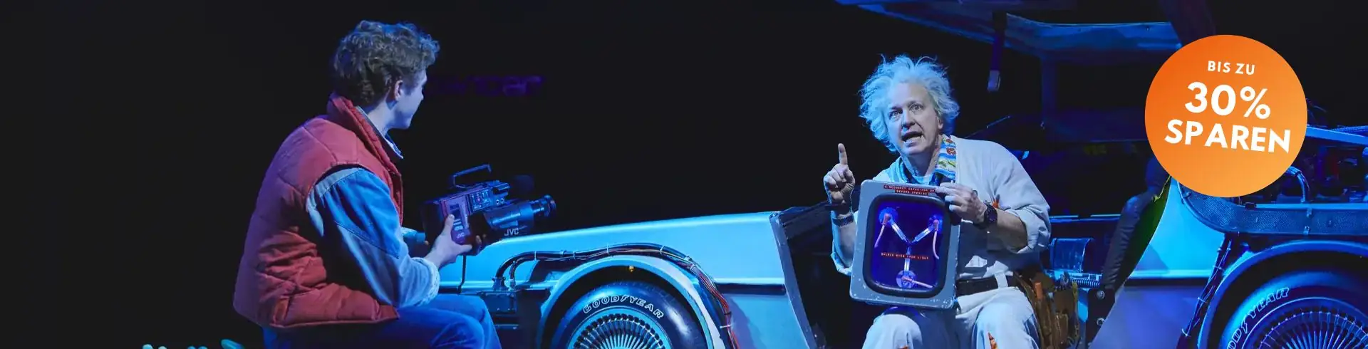 Zwei Schauspieler in Kostümen sitzen vor einem DeLorean-Auto auf einer Bühne, rechts ein orangefarbener Kreis mit dem Text 'BIS ZU 30% SPAREN'
