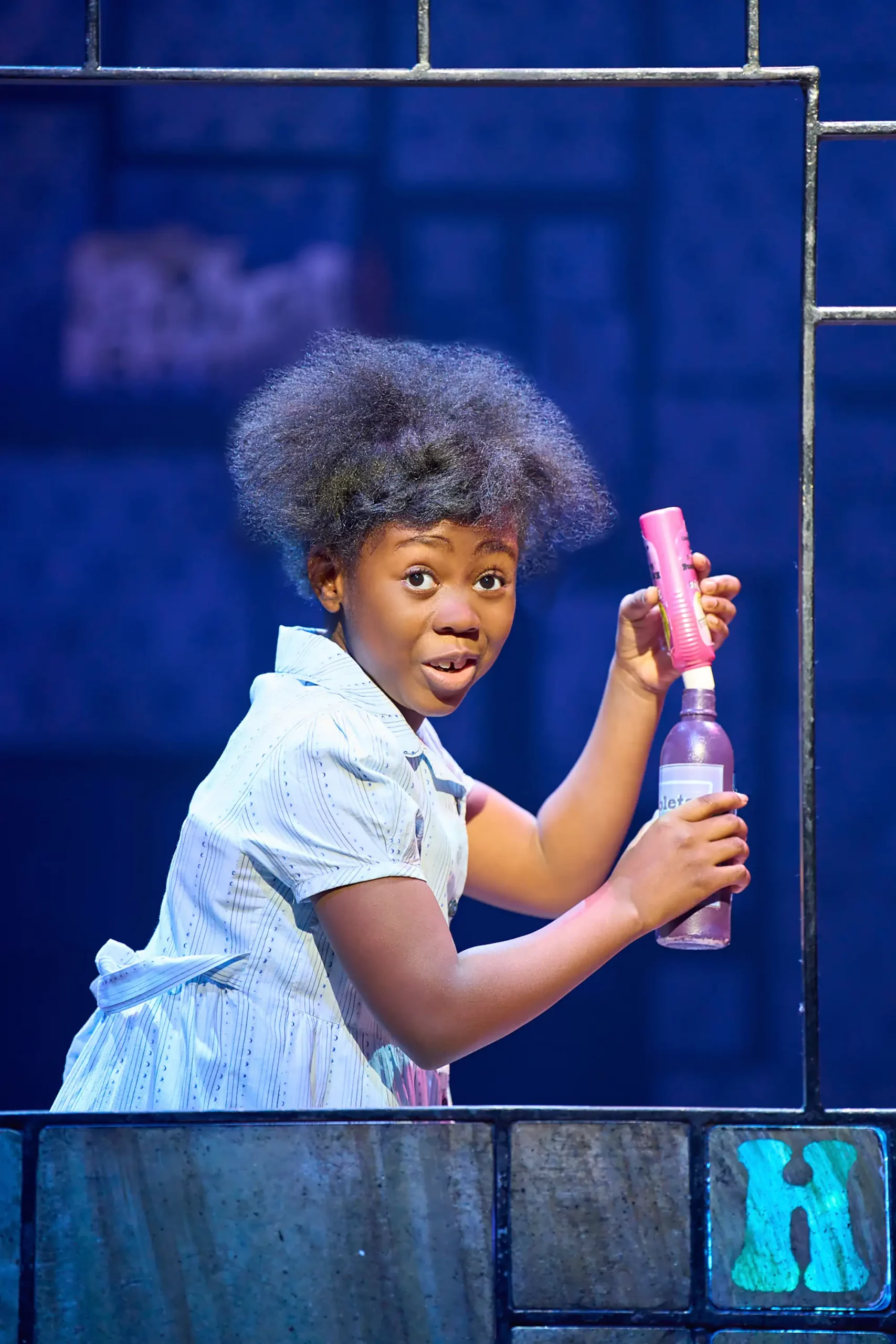 Foto der Kinderdarstellerin Heidi Williams als Matilda welche in der Hand zwei Flaschen übereinander hält