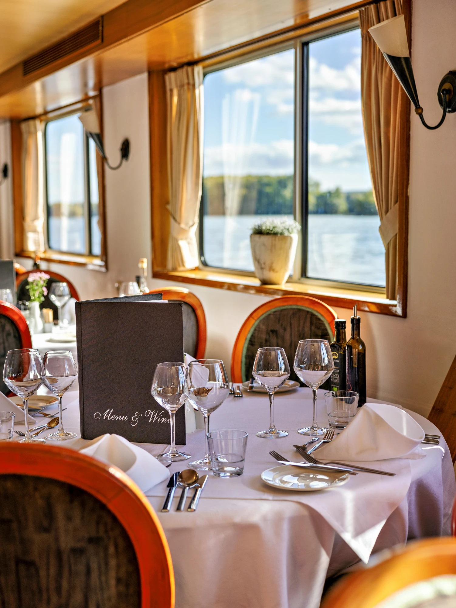 Restaurant der MS Olympia mit gedeckten Tischen mit Gläsern und Besteck und Speisekarten vor Fenstern