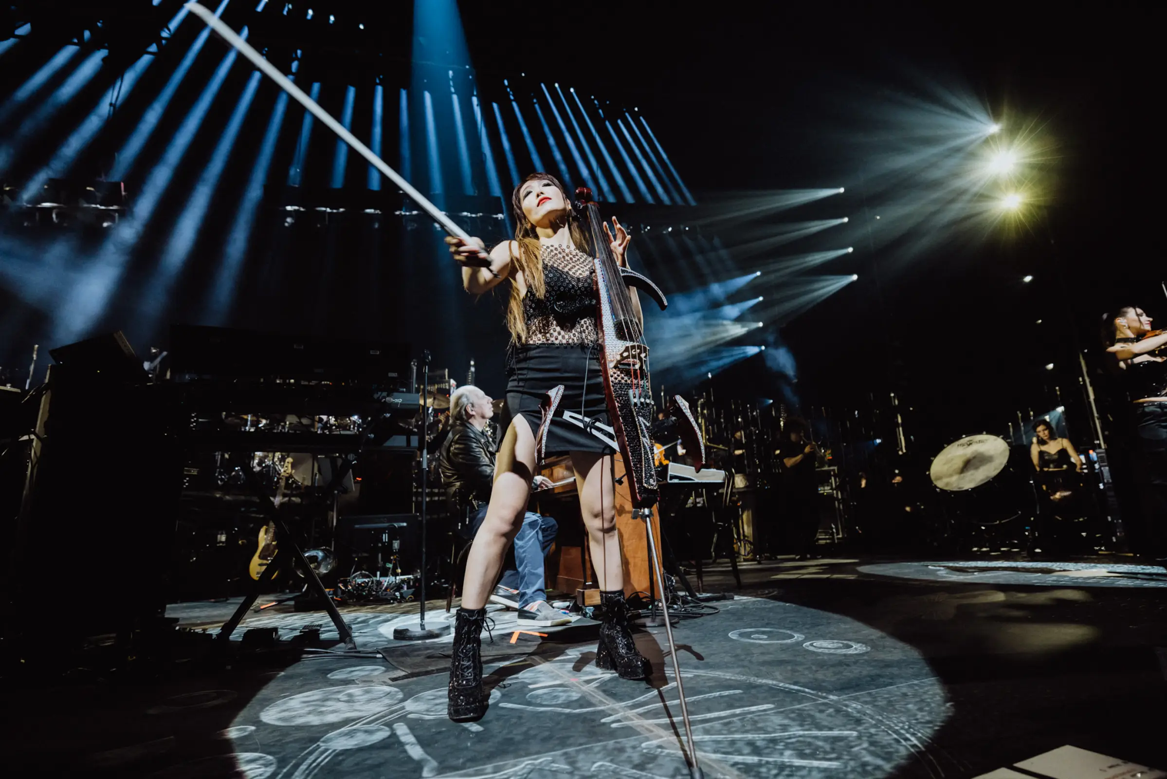 Eine Cellistin performt leidenschaftlich auf der Bühne während der Hans Zimmer Show, umgeben von dramatischen Lichteffekten und einem Orchester im Hintergrund. Die dynamische Inszenierung verstärkt die Intensität des musikalischen Erlebnisses.