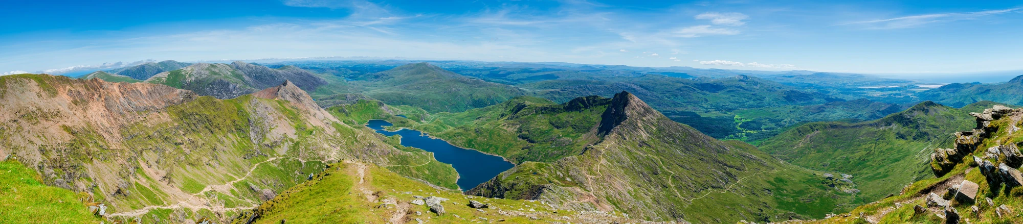 Panoramablick auf grüne Berge und einen See unter blauem Himmel in Wales