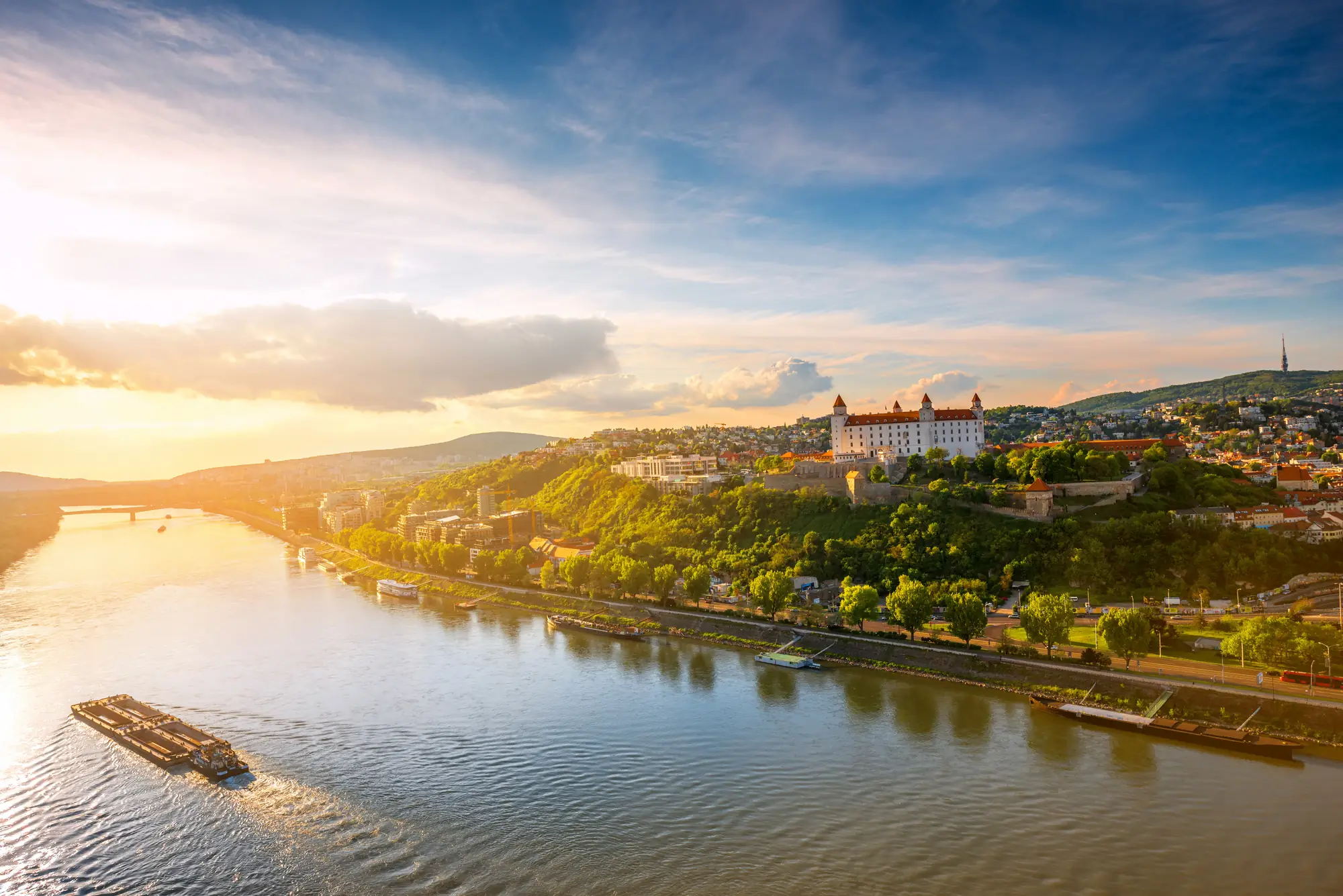 Fluss mit einem Frachtschiff und einer Burg auf einem bewaldeten Hügel bei Sonnenuntergang