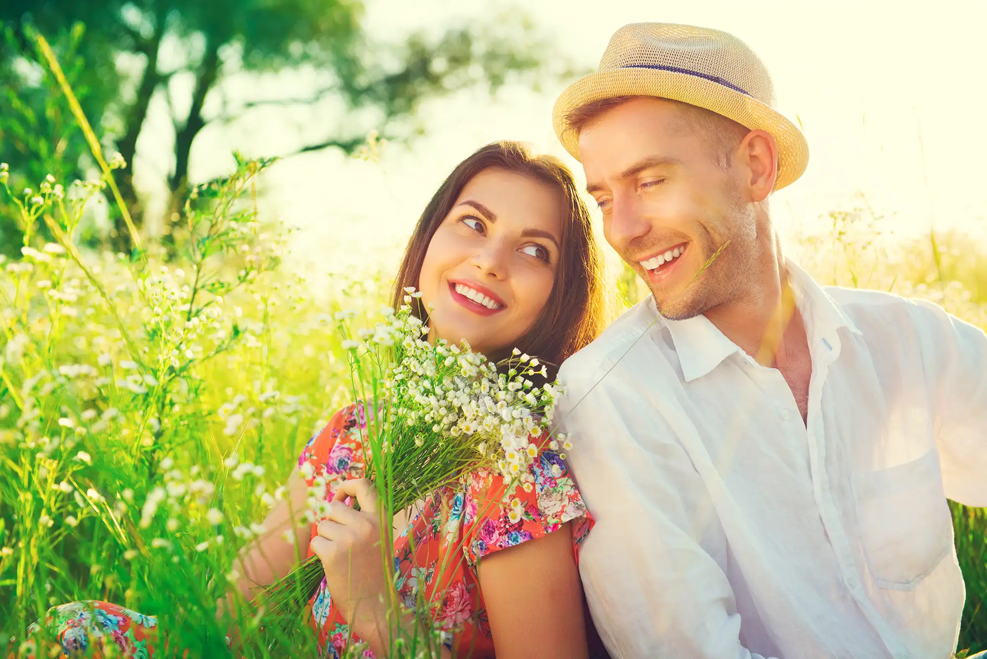 Geschenkidee - Junges Paar auf einer Wiese sitzend mit einem Blumenstrauß in der Hand