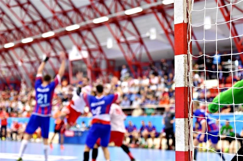 Nahaufnahme eines Handballtors mit unscharfem Hintergrund von Spielern in Aktion in einer Halle mit Zuschauern.