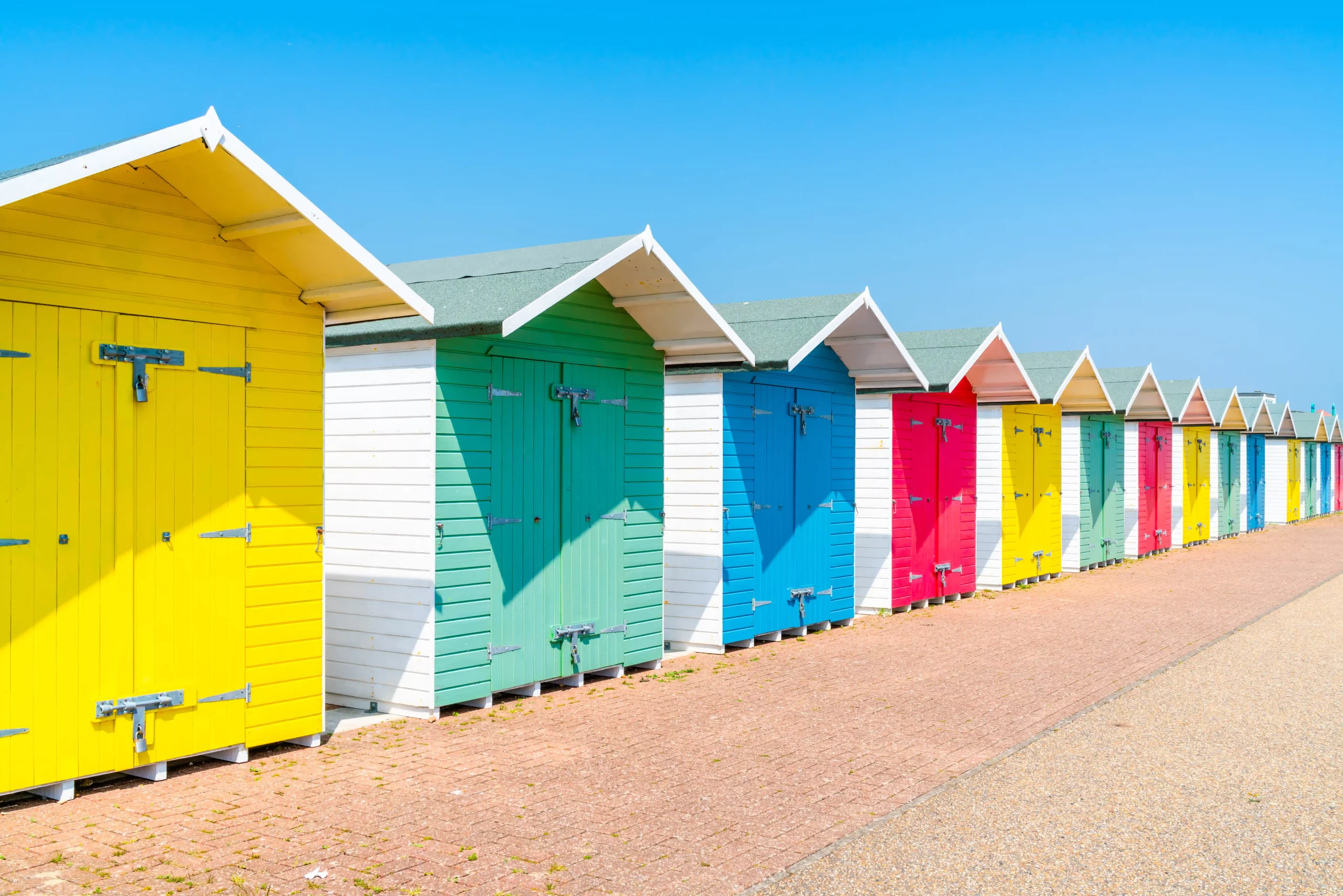 Eine Reihe von bunten Strandhütten in lebhaften Farben, die am Strand aufgereiht sind.