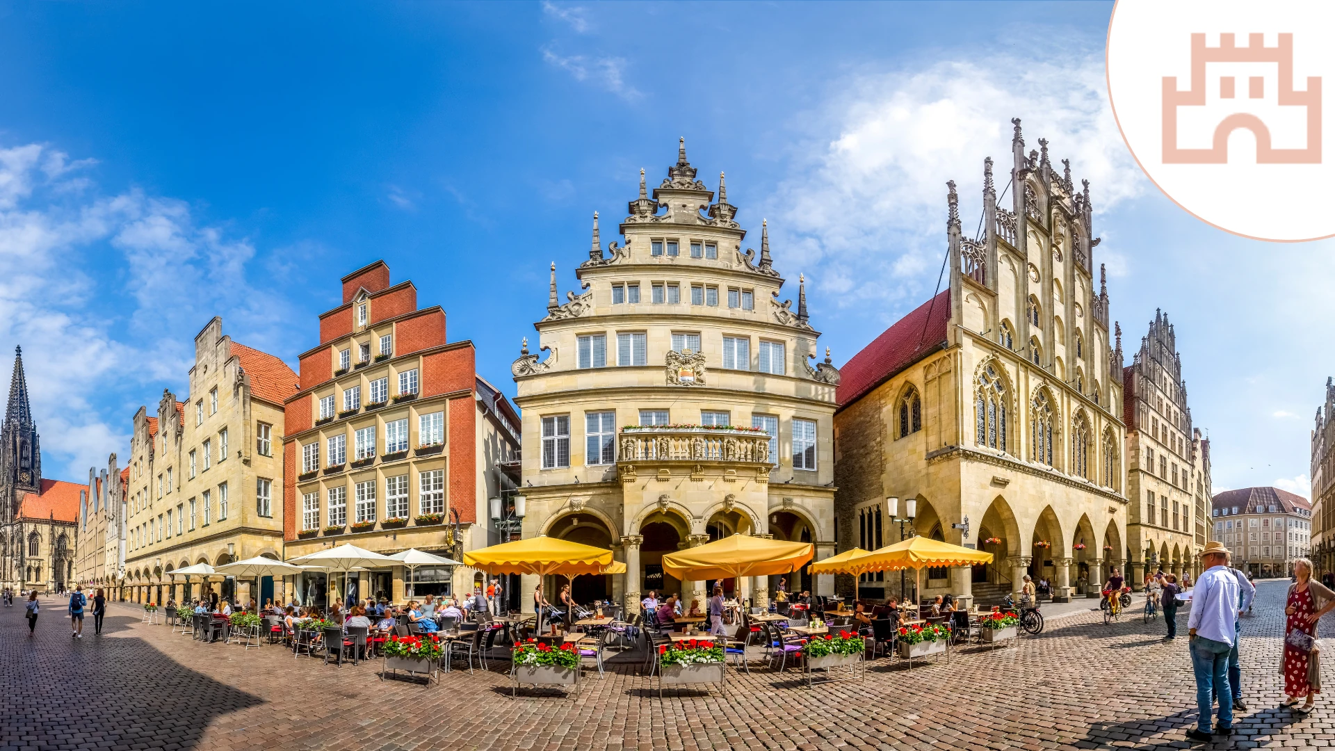 Das Bild zeigt eine lebendige Szene aus der Altstadt von Münster. Im Vordergrund befindet sich ein Marktplatz mit gemütlichen Straßencafés, gelben Sonnenschirmen und blühenden Blumenarrangements. Umgeben wird der Platz von historischen Gebäuden mit prachtvollen Fassaden, darunter das imposante Rathaus von Münster mit seiner gotischen Architektur. Der Himmel ist blau mit einigen weißen Wolken, was der Szene eine freundliche und einladende Atmosphäre verleiht.