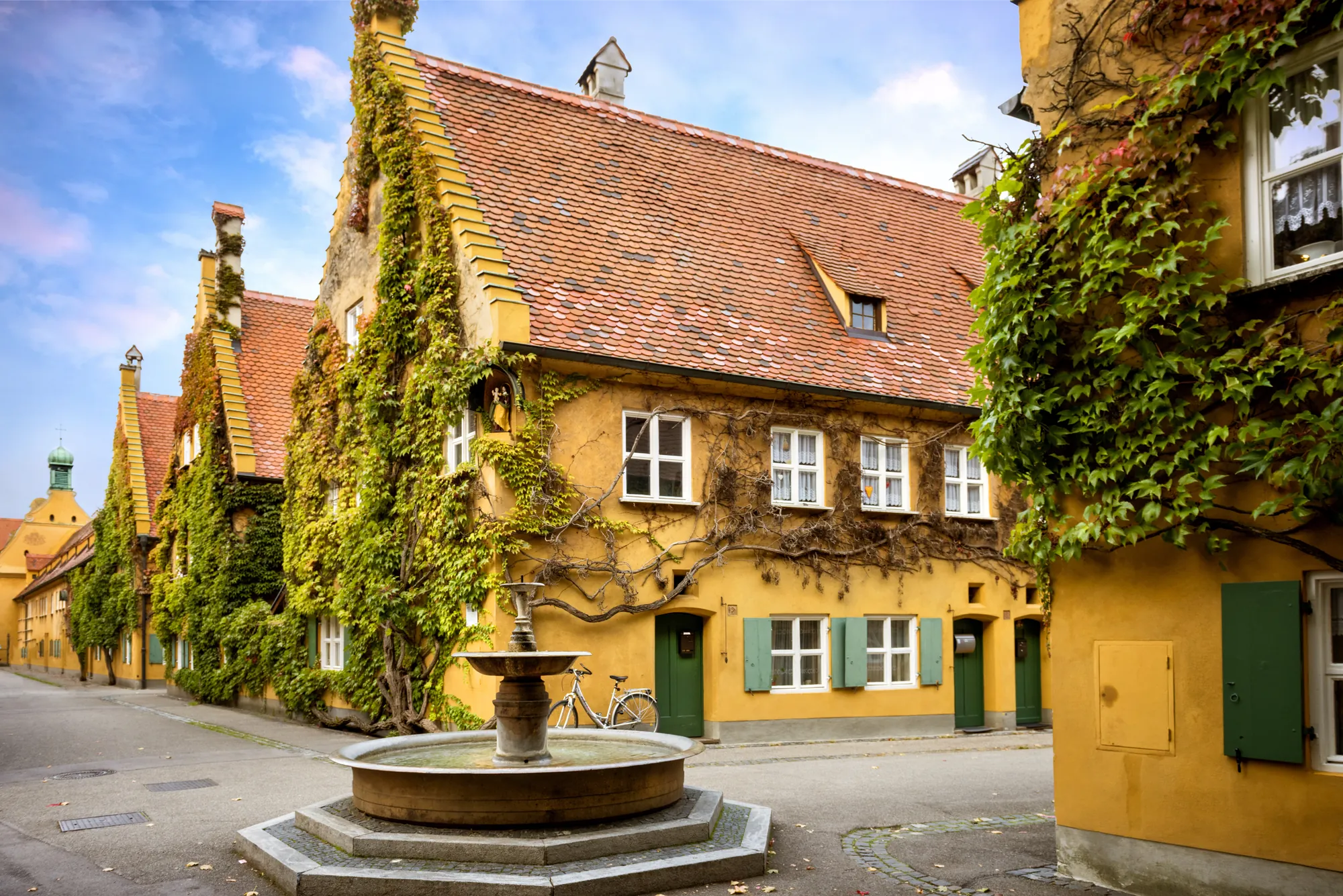 Die historische Fuggerei in Augsburg mit ihren gelb gestrichenen und von Weinlaub umrankten Häusern