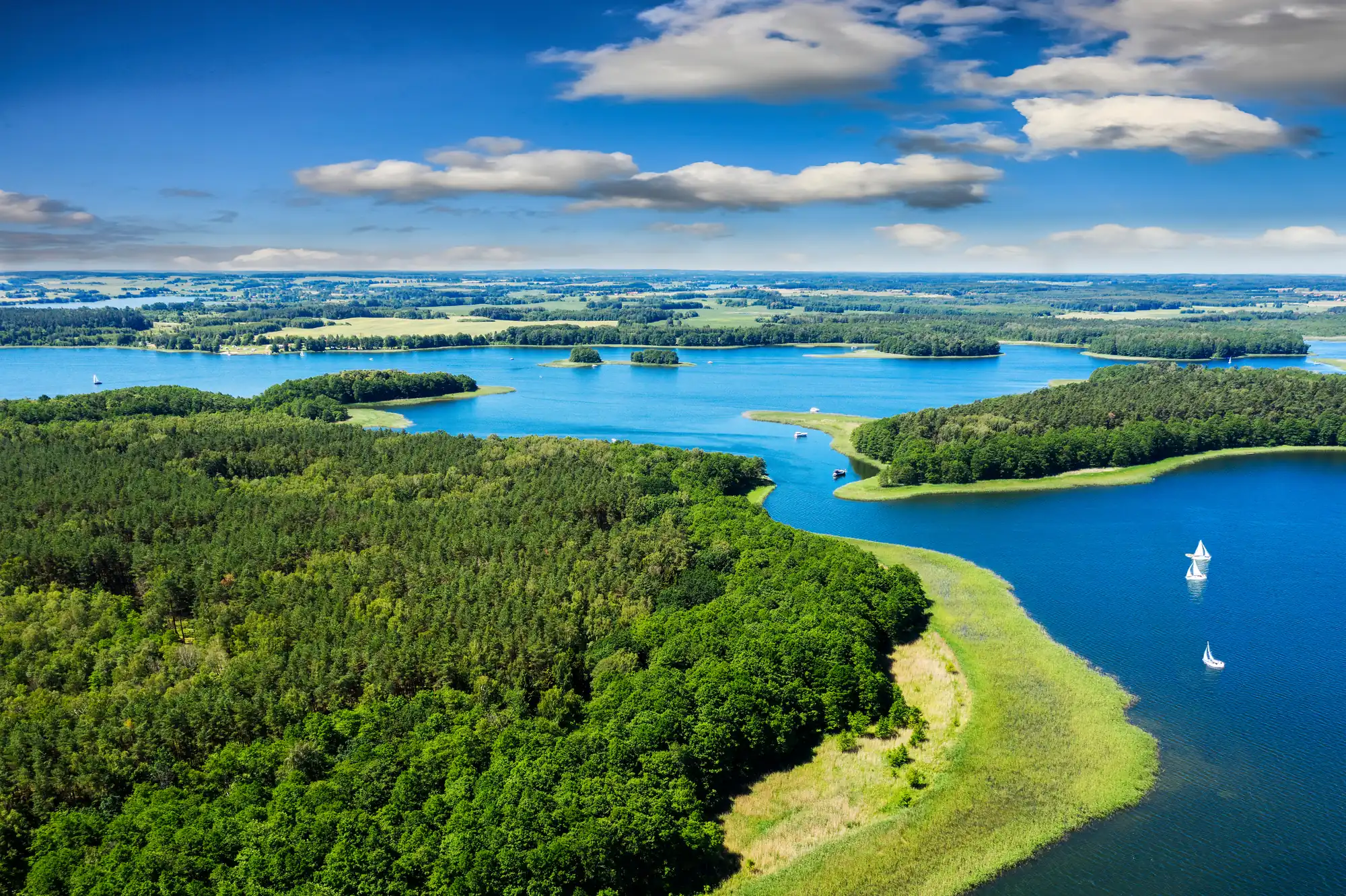 Luftaufnahme eines großen Sees mit mehreren bewaldeten Inseln und Segelbooten unter blauem Himmel mit Wolken -Masuren Polen