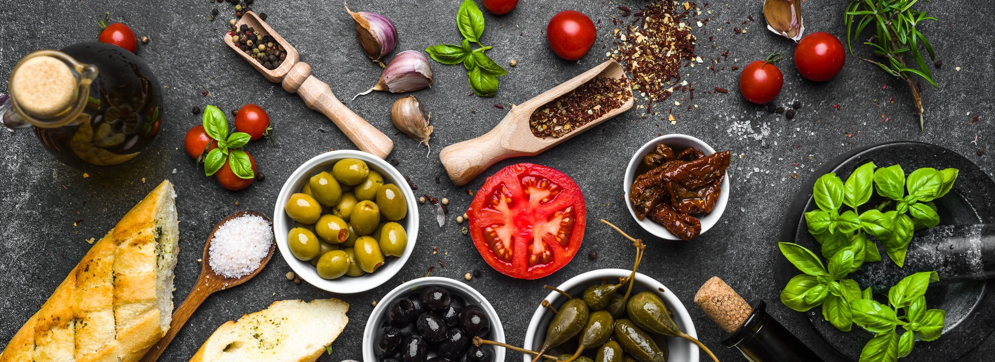 Antipasti-Vorbereitung mit grünen und schwarzen Oliven, Tomaten, Essig und Öl, Knoblauchbrot, Basilikum, Thymian, Knoblauch, Pfeffer und Salz.