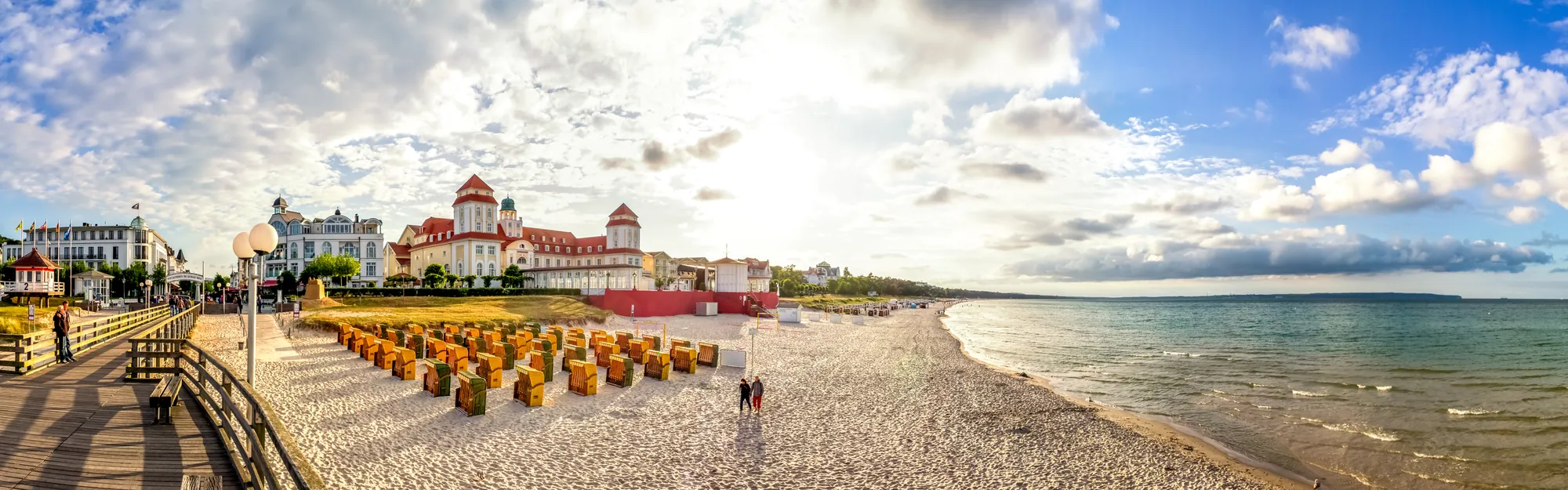 Belebte Promenade am Strand mit Gästen und historischen Gebäuden.