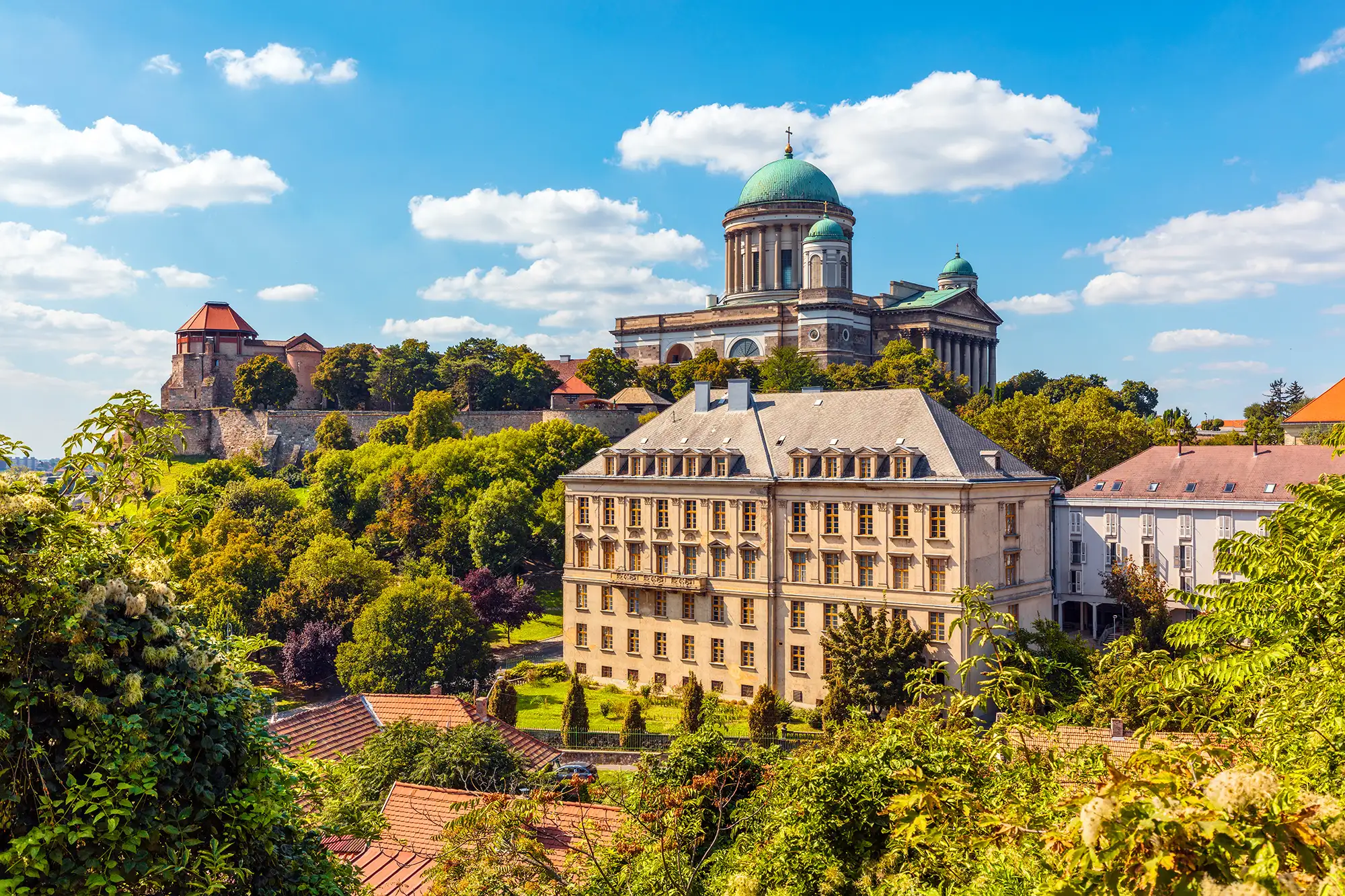 Sankt-Adalbert-Kathedrale und Basilika in Esztergom auf einem Berg mit Bäumen und Stadtmauer im Vordergrund