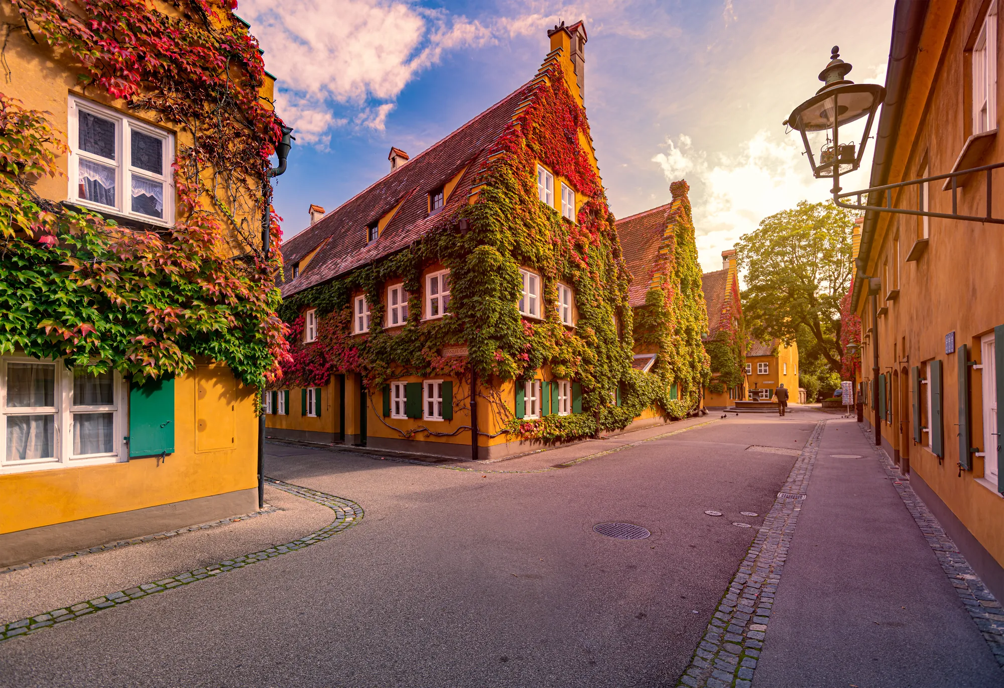 Die historische Fuggerei in Augsburg mit rötlich-grünen Weinlaub in der Morgensonne