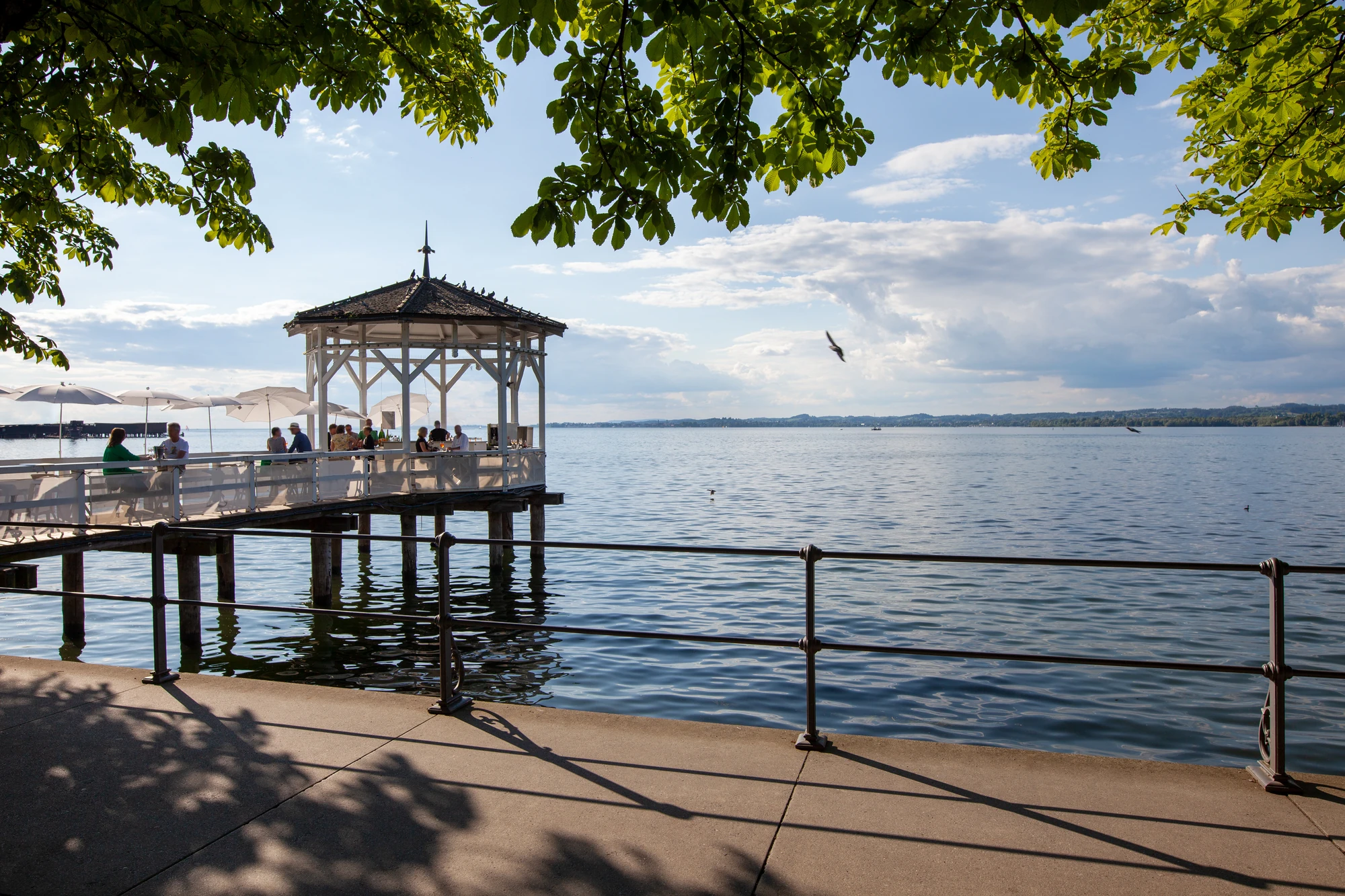 Malerische Seelandschaft mit einem Pavillon und grünen Bäumen im Vordergrund.