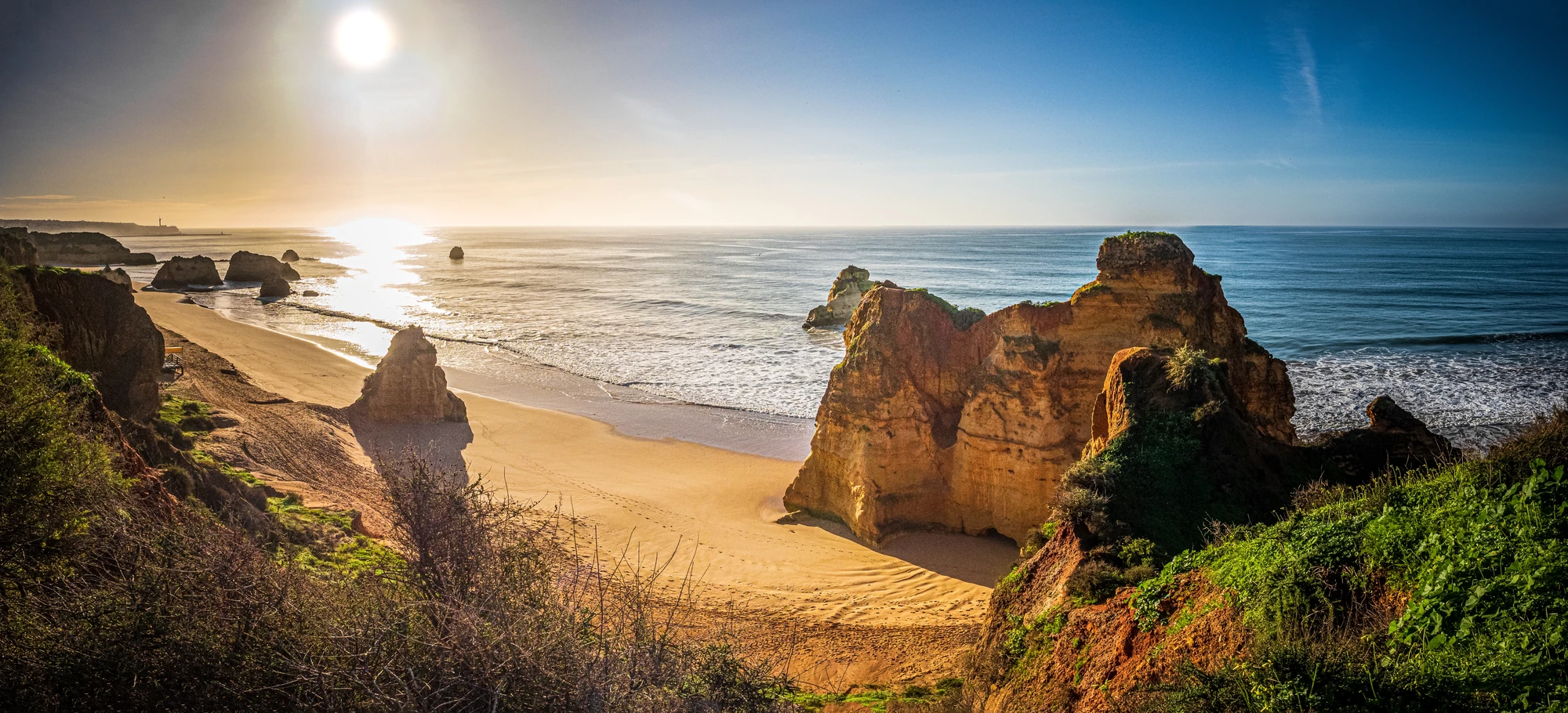 Felsformationen und Sandstrand an der Küste bei Sonnenaufgang mit ruhigem Meer und klarem Himmel.- Algarve Portimão