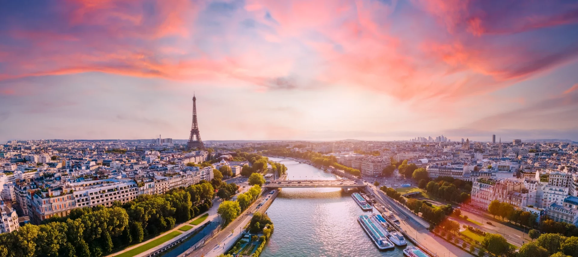 Panoramablick über Paris, der die Seine zeigt, mit dem Stadtbild entlang der beiden Ufer und dem Eiffelturm in der Ferne, unter einem leicht rötlichen Himmel.