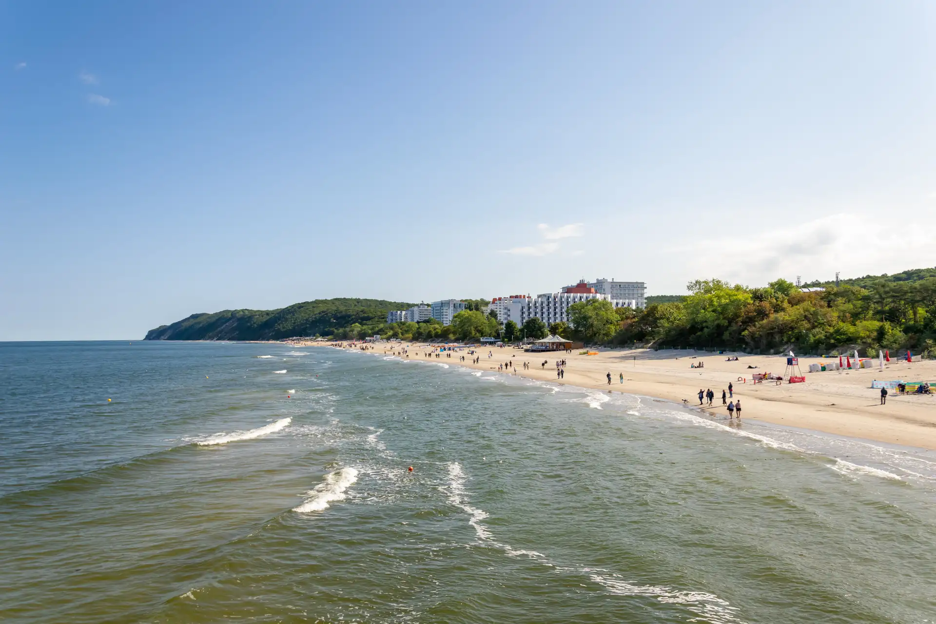 Menschen spazieren am Strand von Misdroy mit Häusern und Bäumen entlang der Küstenlinie
