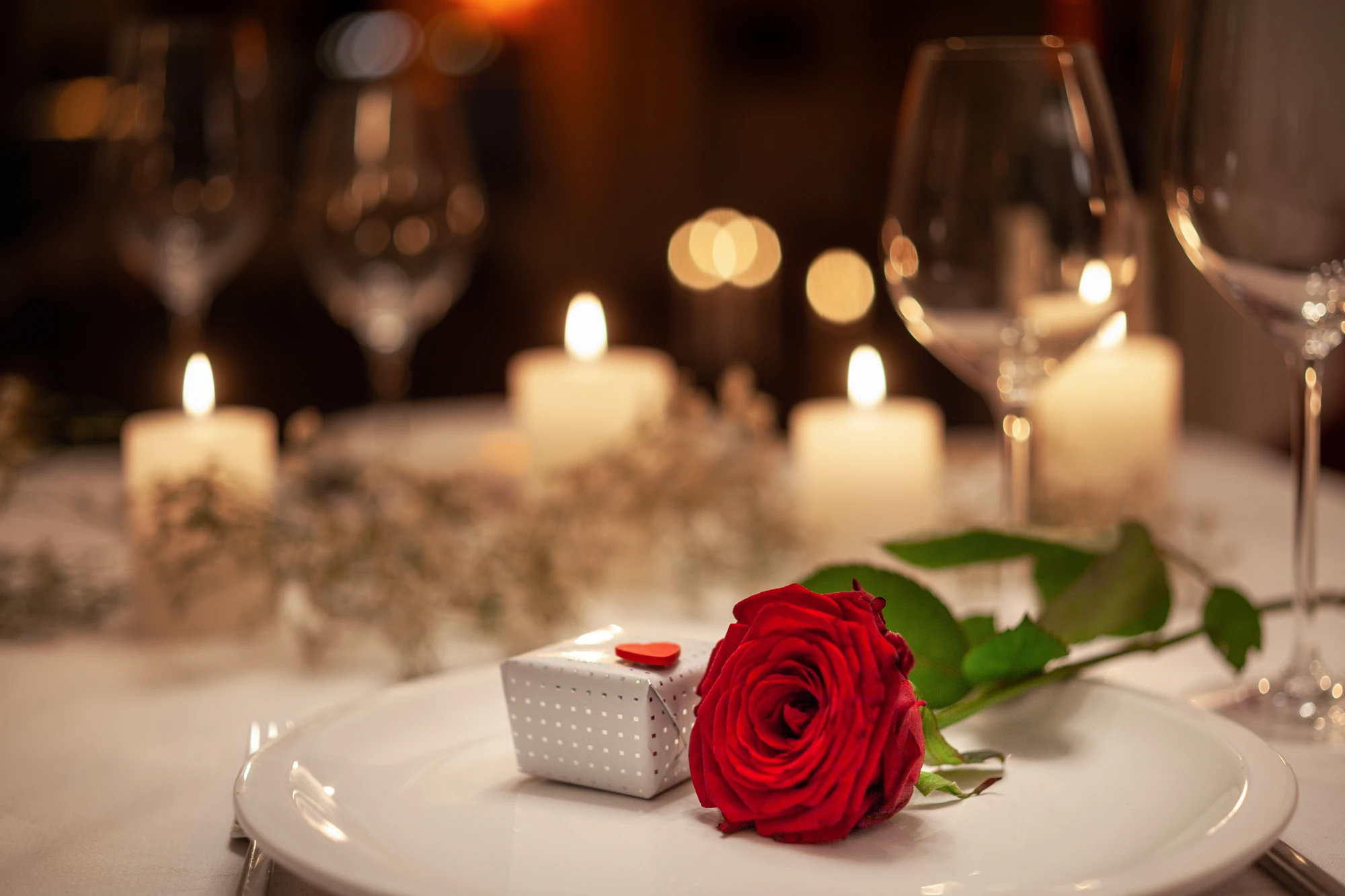 eine Rose mit kleinem Geschenk auf Restauranttisch mit Teelichtern im Hintergrund