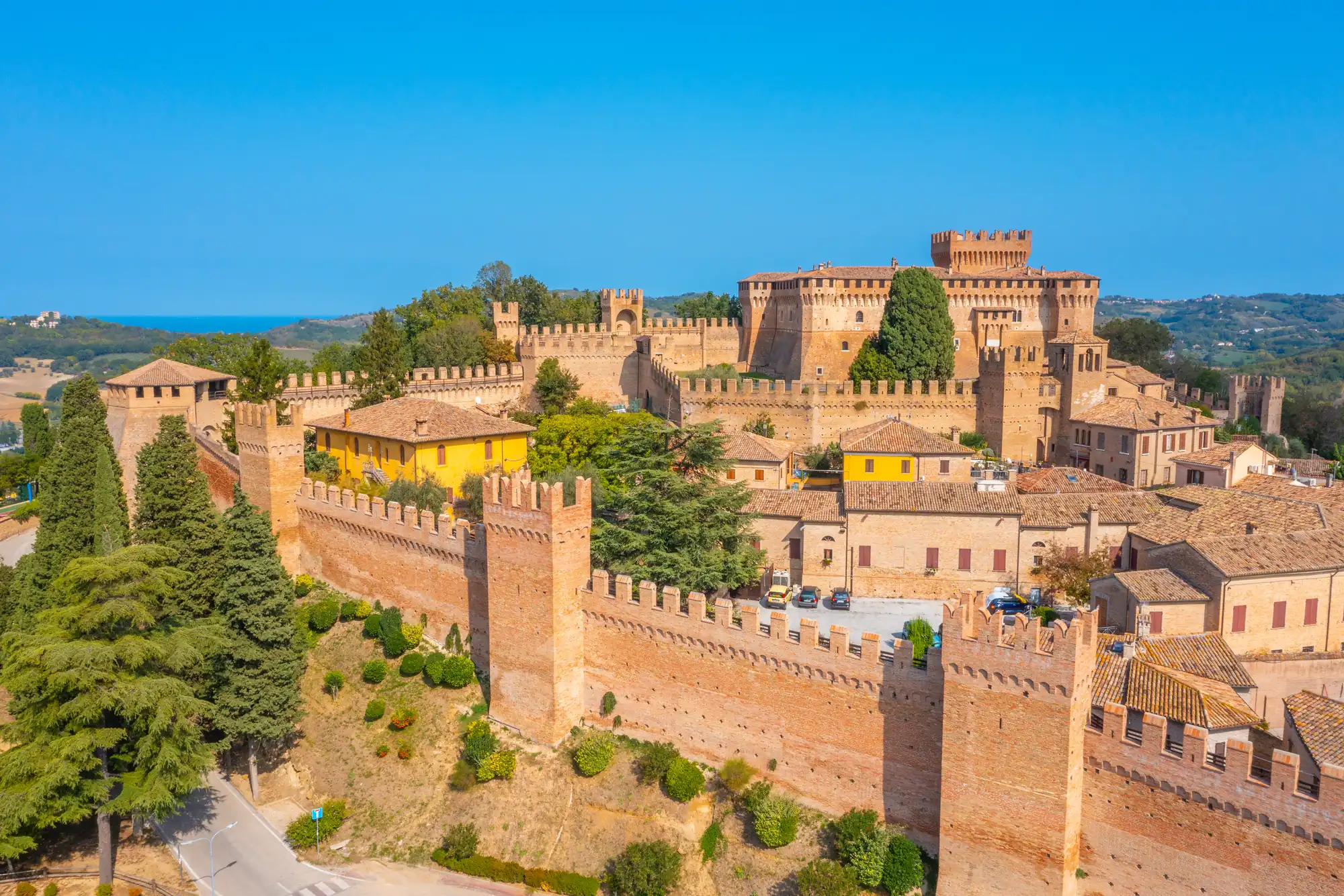 Italien / Schmale Kopfsteinpflasterstraße in einer italienischen Stadt mit vielen weißen Tauben, umgeben von historischen Gebäuden und einer Burg im Hintergrund