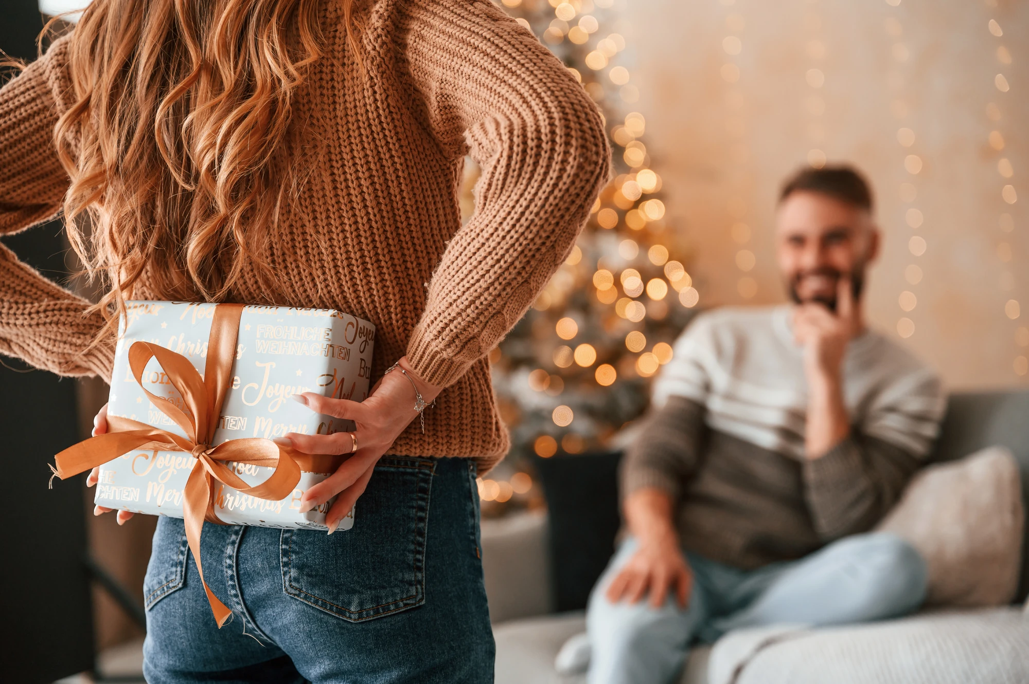 Pärchen Geschenke - Frau hält Geschenk hinter dem Rücken, Mann guckt sie glücklich an