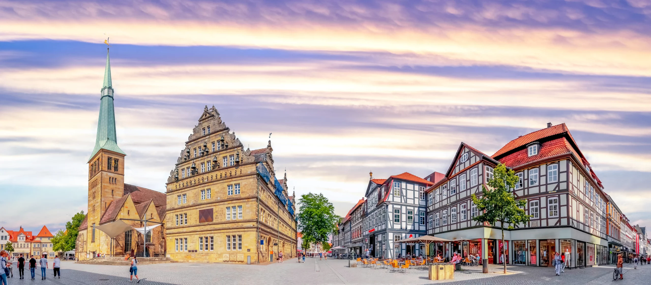 Marktplatz in Hameln mit Fachwerkhäusern, einem historischen Rathaus mit Treppengiebel und einer Kirche mit hohem Turm im Hintergrund bei bewölktem Himmel
