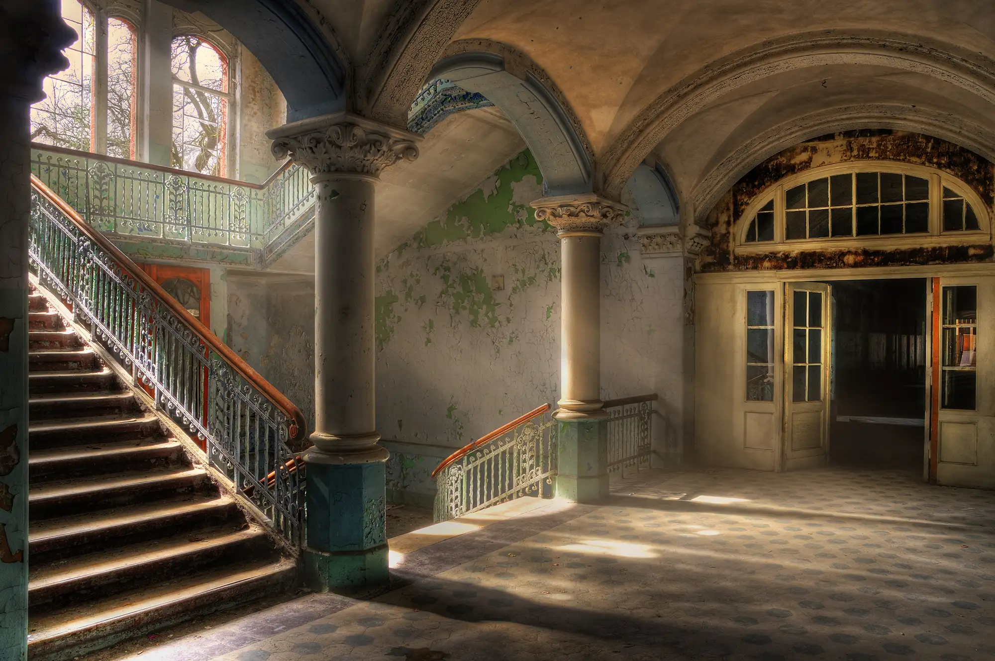 Treppen und Treppengeländer in den Beelitz Heilstätten mit abgeblätterten Wänden und Türen und Torbogen