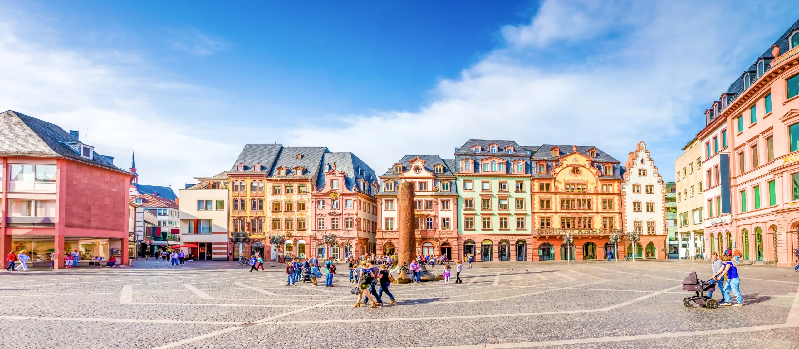 Blick auf den Domplatz in Mainz mit Häuserfassaden im Hintergrund bei gutem Wetter mit Menschen, die über den Platz schlendern.