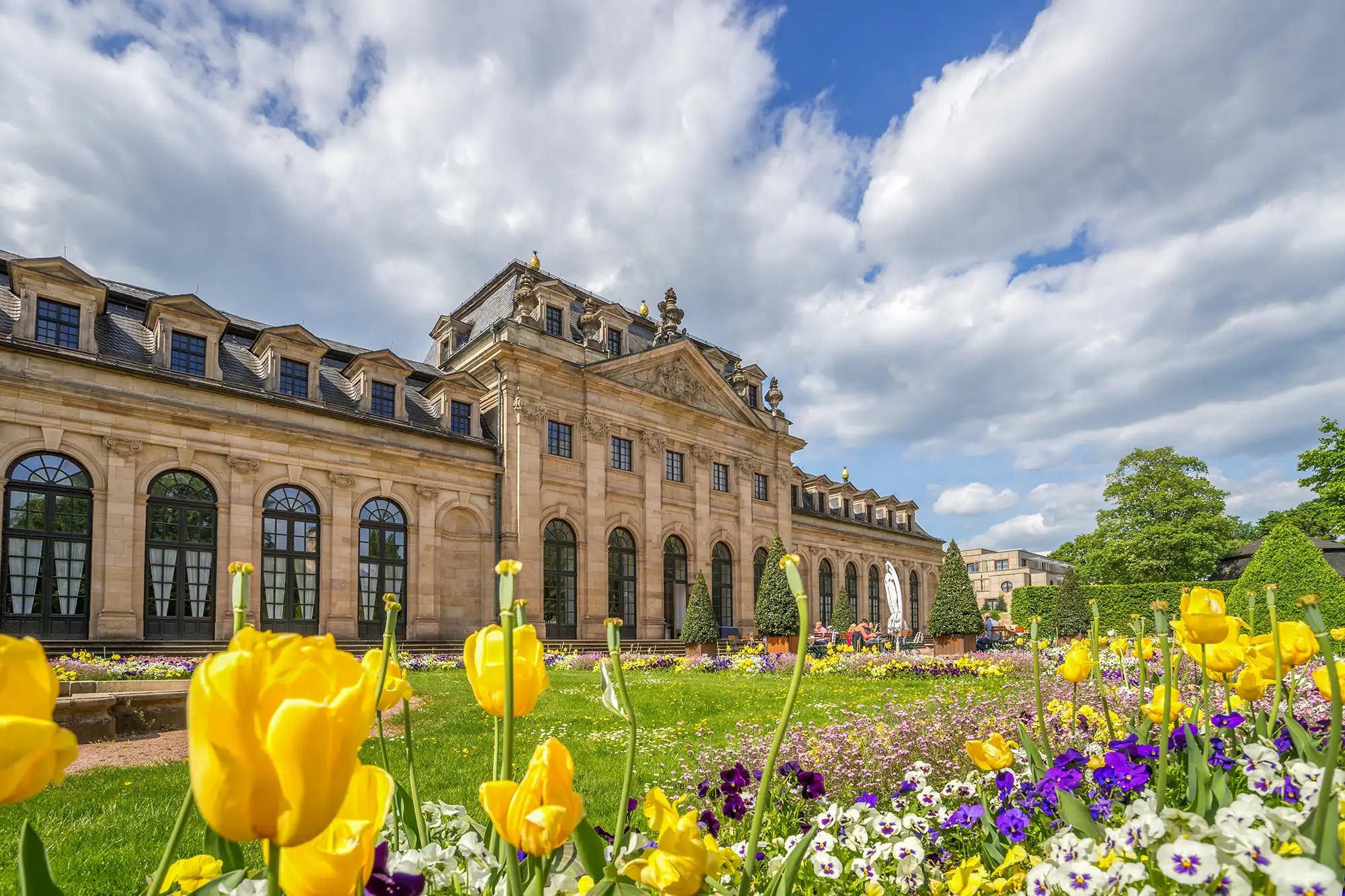 Orangerie in Fulda mit Grünflächen Blumen und Bäumen bei blauem Himmel mit wolken