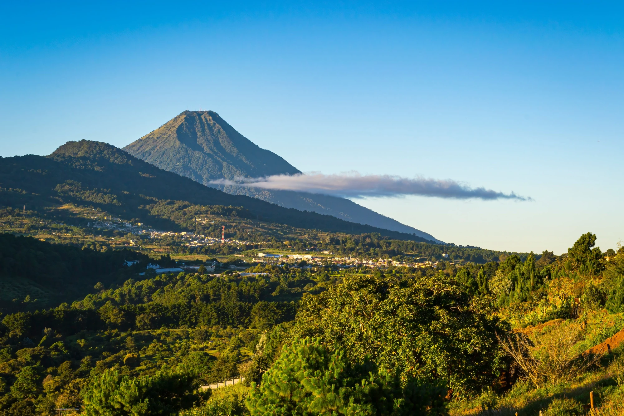 Grüne Berglandschaft mit einem Vulkan im Hintergrund.