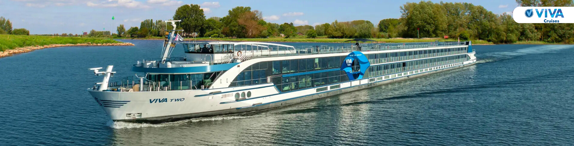 Flusskreuzfahrtschiff VIVA TWO fährt auf einem Fluss mit einer Stadt und einem bewaldeten Hintergrund