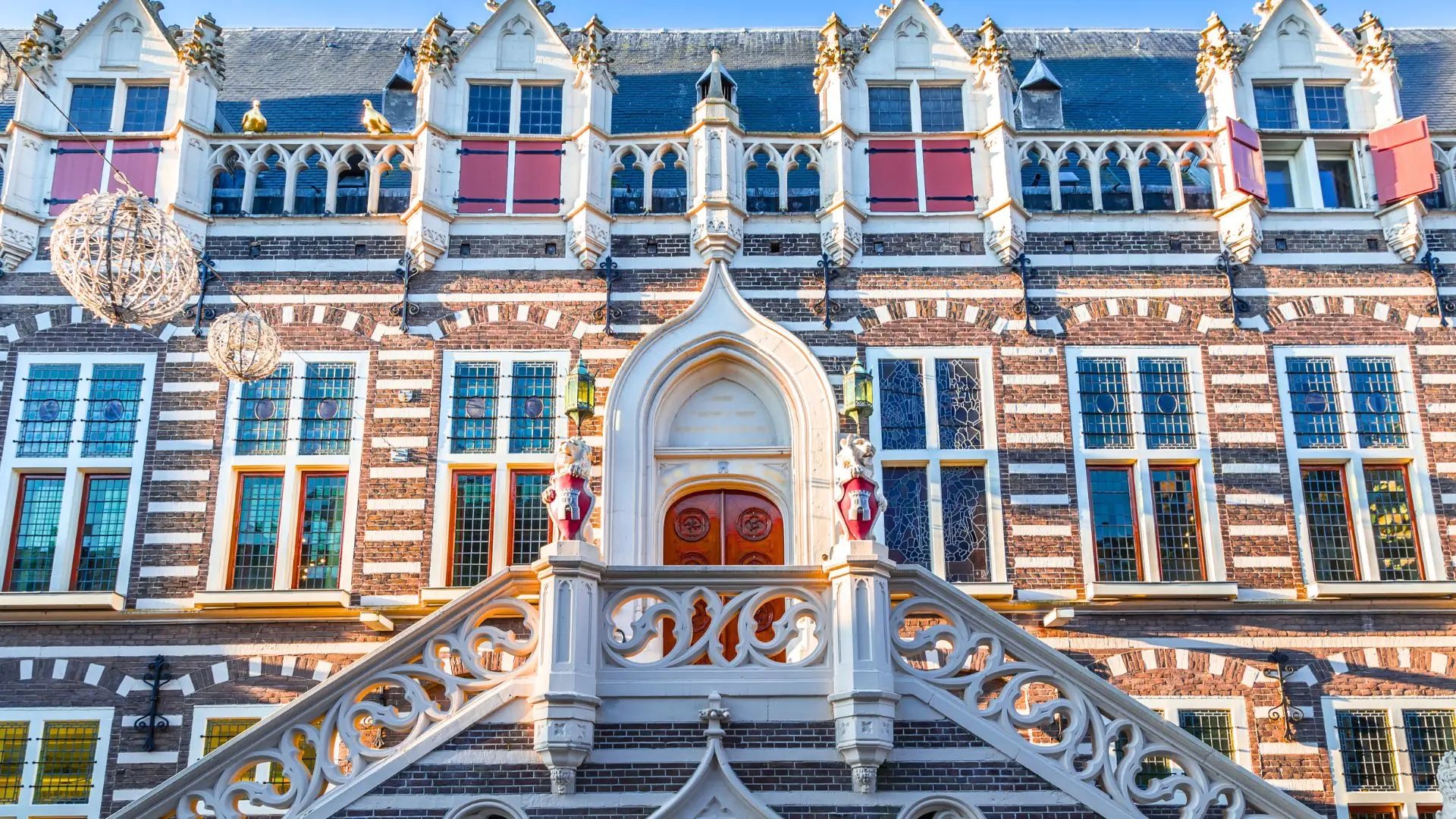 Fassade des Rathauses Alkmaar mit roten Fensterläden, verzierten weißen Steinelementen und einer geschwungenen Treppe zum Eingang mit Holzportal.