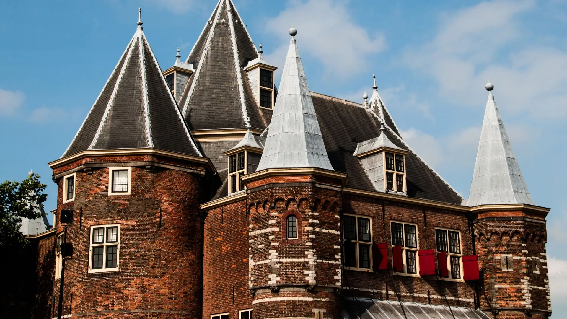 Gebäude Waaggebouw in Alkmaar mit spitzen Türmen, kleinen Fenstern und roten Fensterläden vor blauem Himmel.