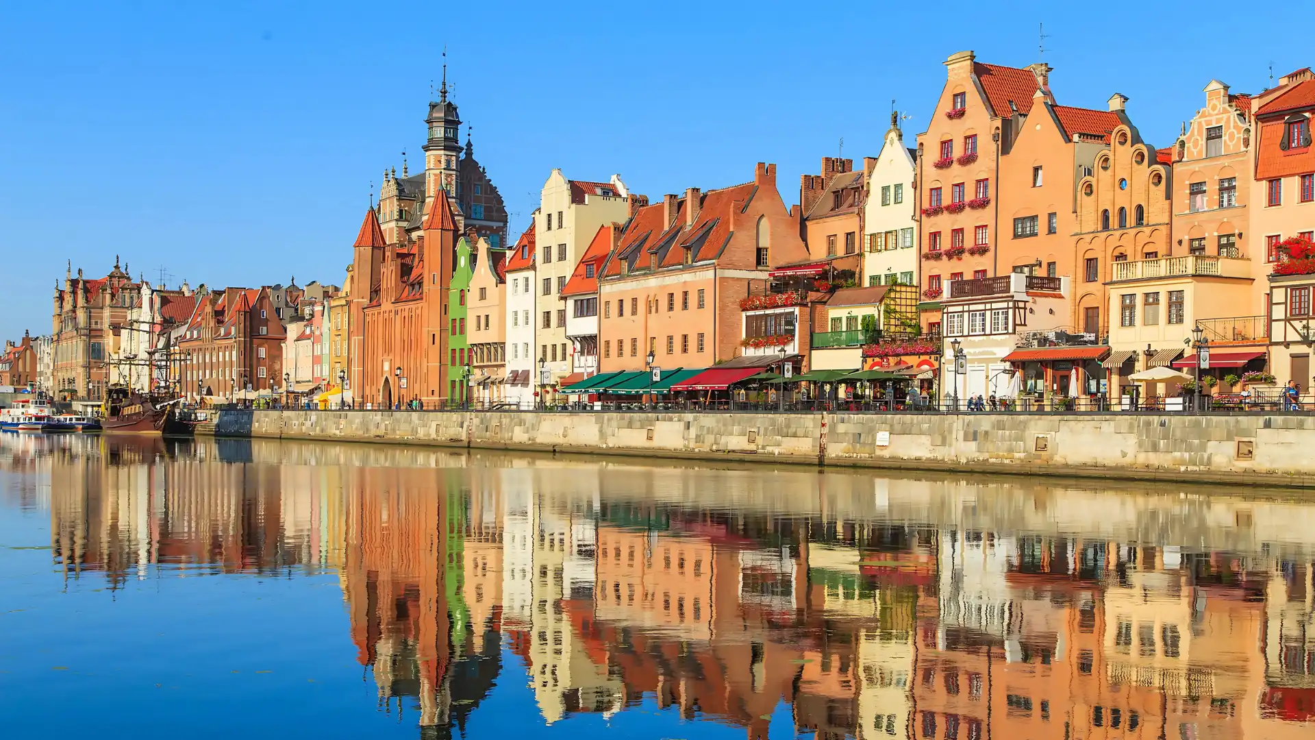 Bunte historische Häuser und Kirchturm am Flussufer in Danzig mit Spiegelung im Wasser bei klarem Himmel