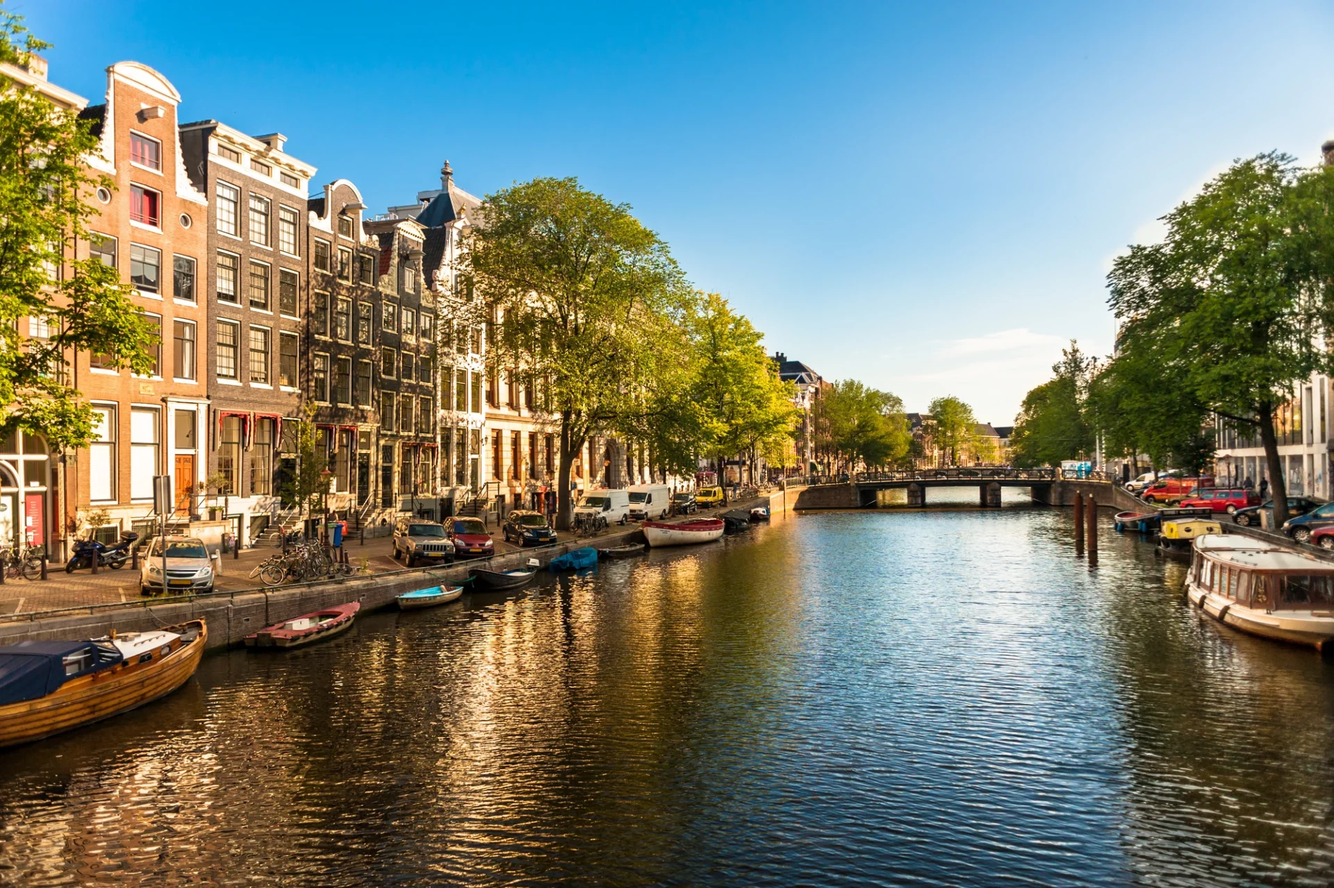 Blick auf den Herengracht-Kanal bei Tageslicht, gesäumt von eleganten Häuserreihen. Angelegte Boote ruhen im Wasser, während die Promenade mit üppigen Bäumen geschmückt ist und eine einladende Atmosphäre schafft.