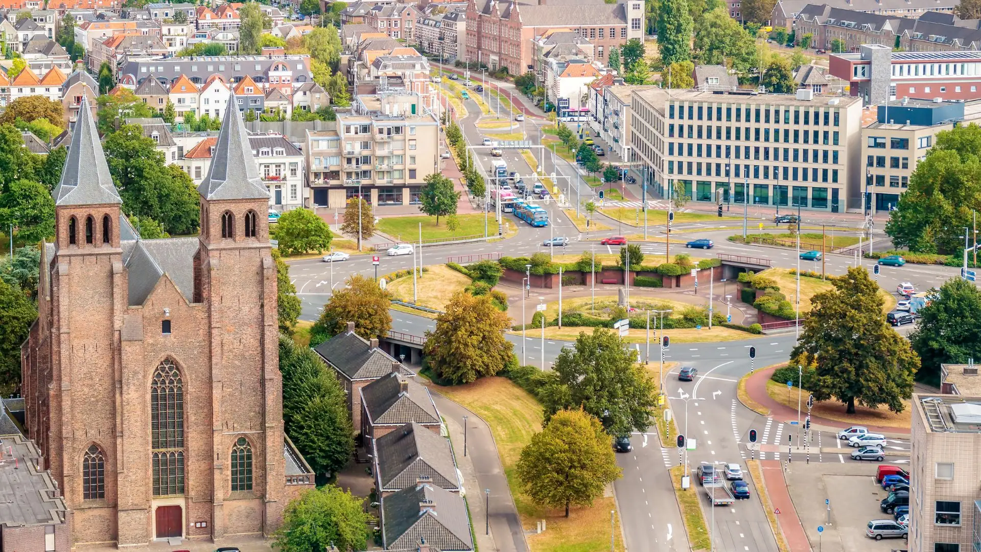 Luftaufnahme von Arnhem mit zwei hohen Kirchtürmen links, Straßen mit Verkehr und mehreren Gebäuden im Hintergrund.