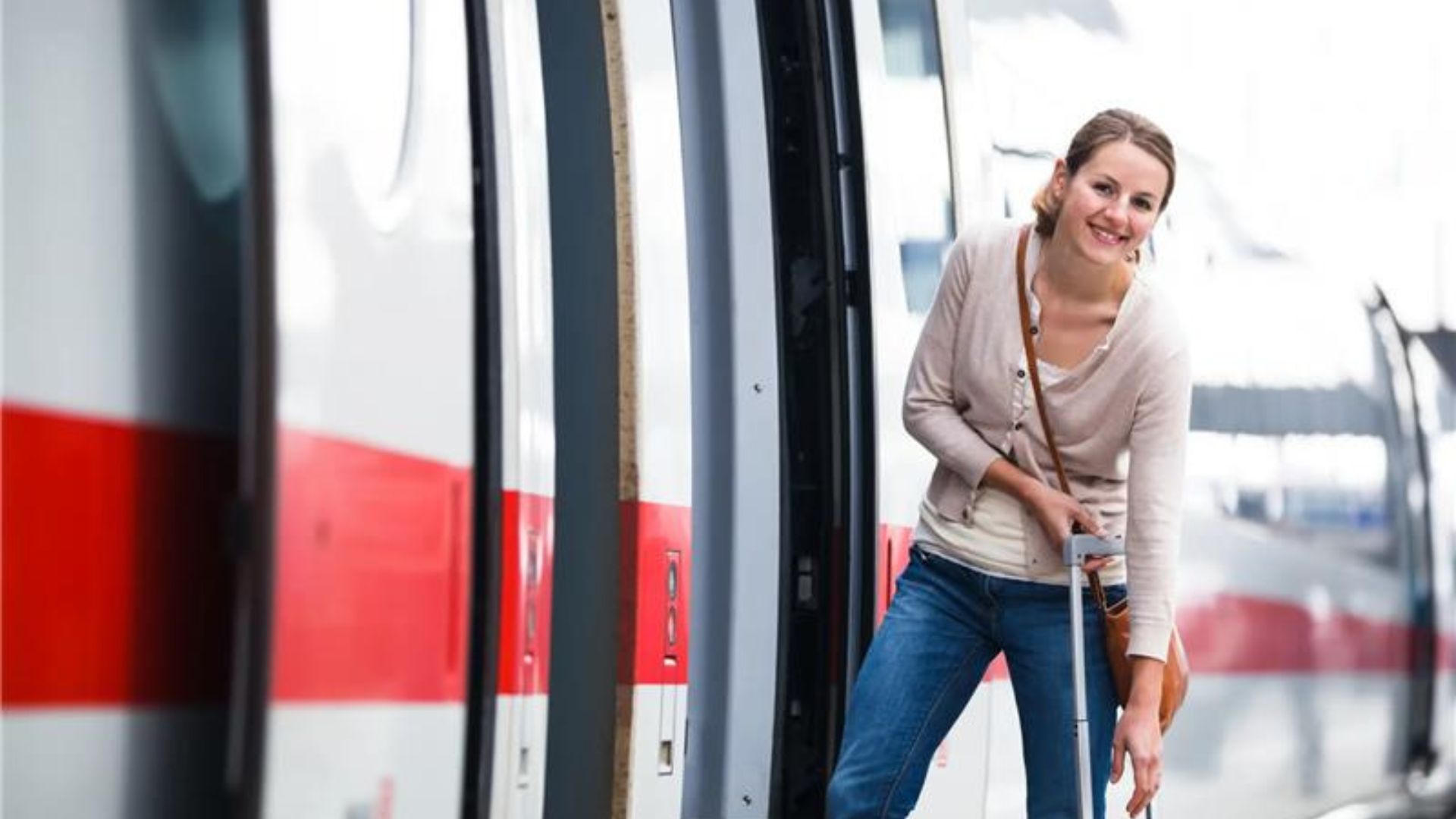 Frau mit beigem Pullover und blauer Jeans steigt in einen weißen ICE mit rotem Streifen ein