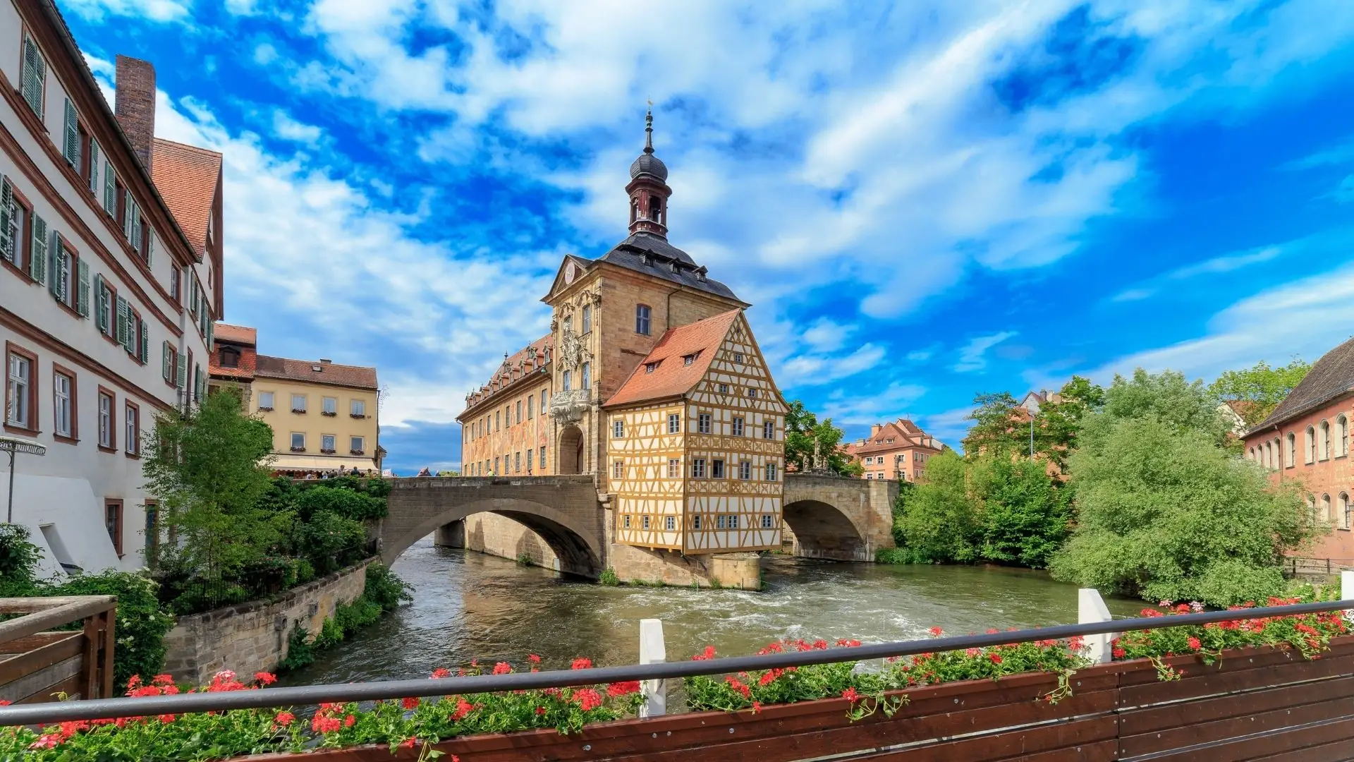 Historisches Rathaus von Bamberg auf einer Brücke über den Fluss Regnitz, umgeben von Fachwerkhäusern und blauem Himmel