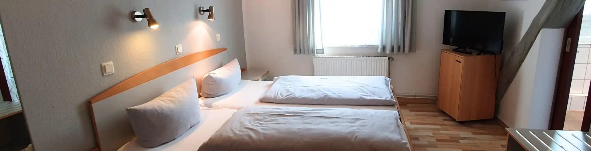 Hotelzimmer mit zwei Einzelbetten, Nachttisch, Wandlampen, Fenster mit Vorhängen und Fernseher auf einem Schrank