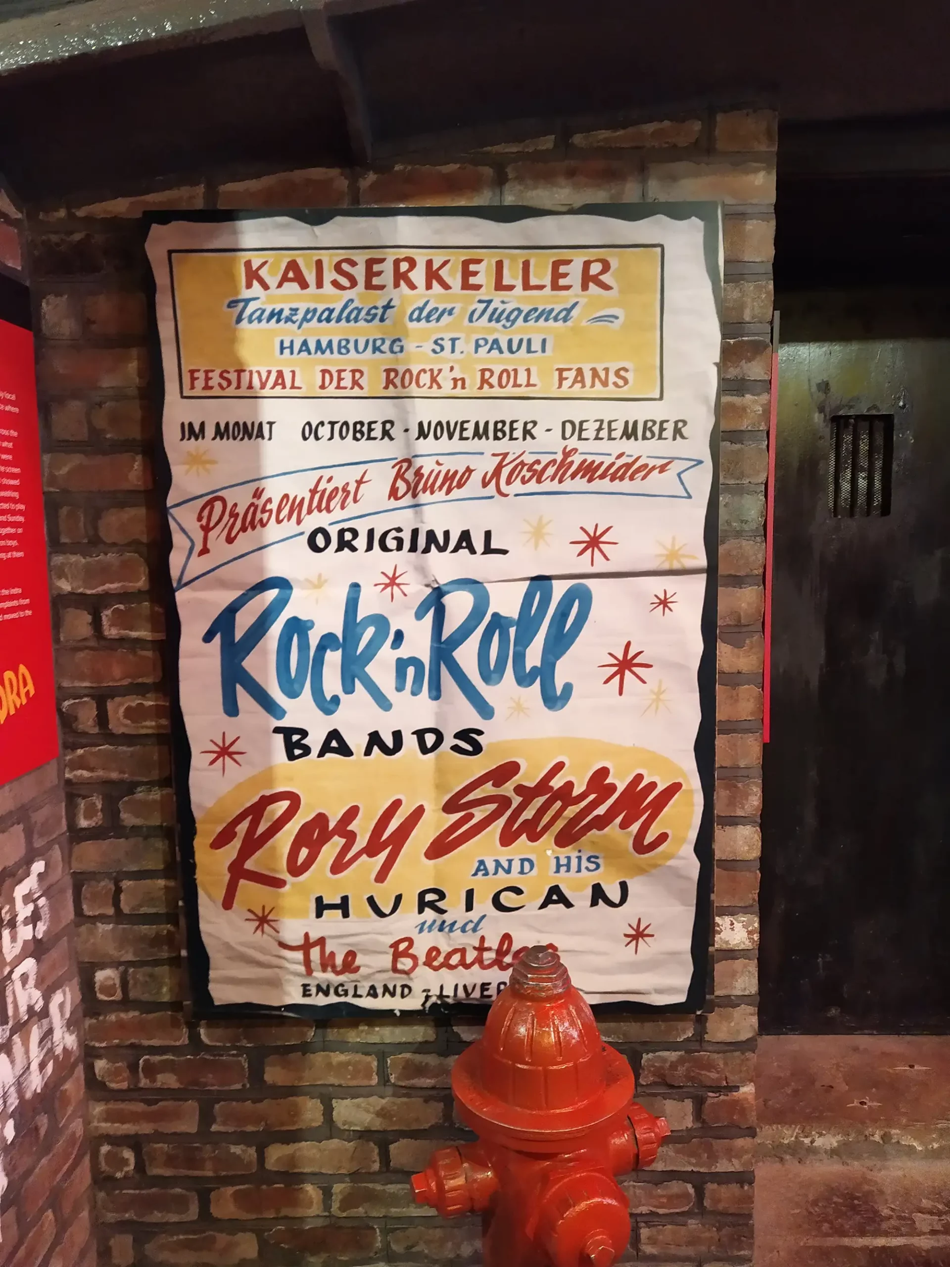 Beatles Museum Liverpool - Plakat vom Kaiserkeller in Hamburg mit bunter Schrift und Werbung für Rock-'n'-Roll und die Bealtes eingerahmt an einer Steinmauer