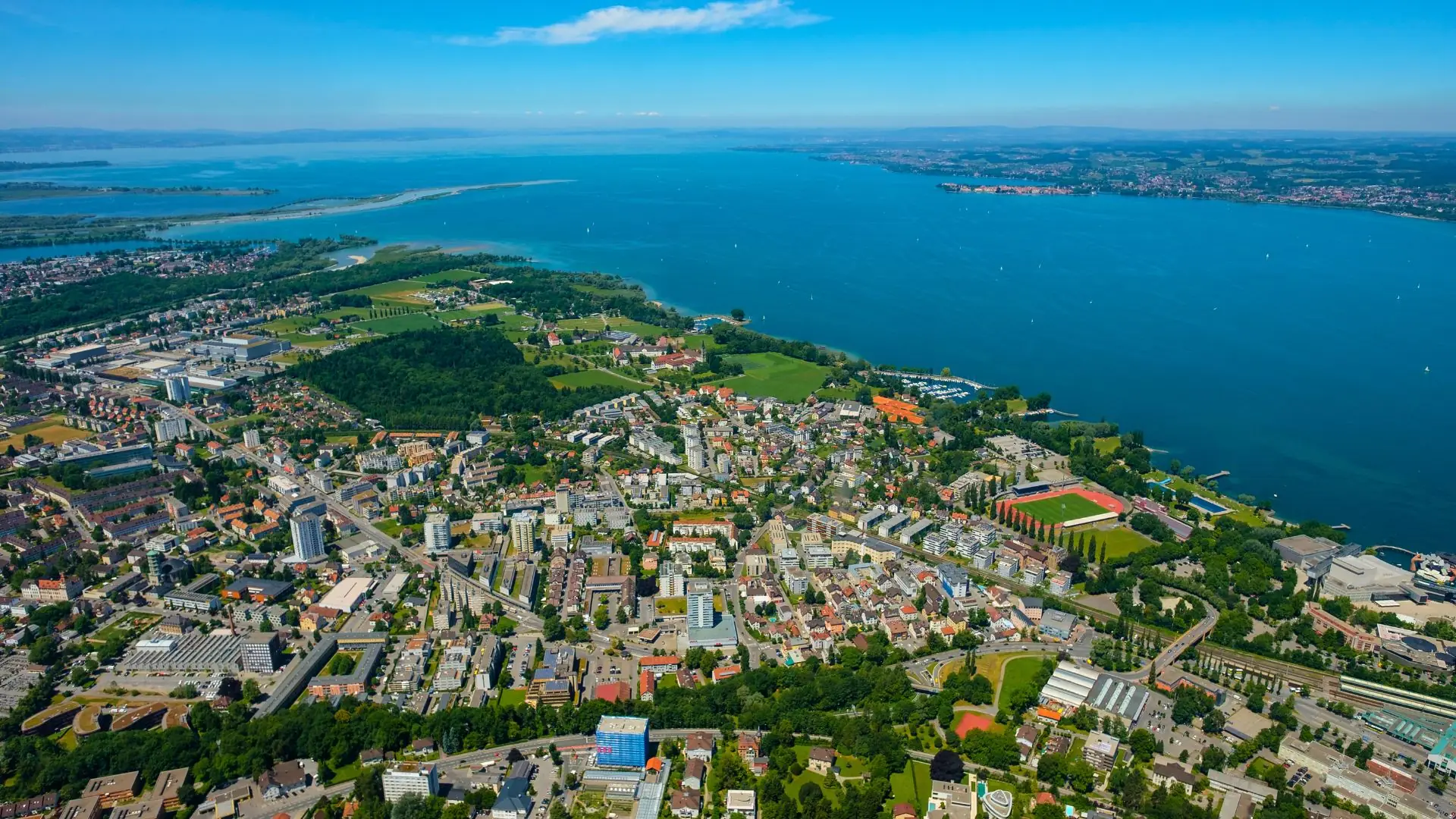 Luftaufnahme von Bregenz mit Stadtgebiet, grünen Flächen und dem Bodensee im Hintergrund
