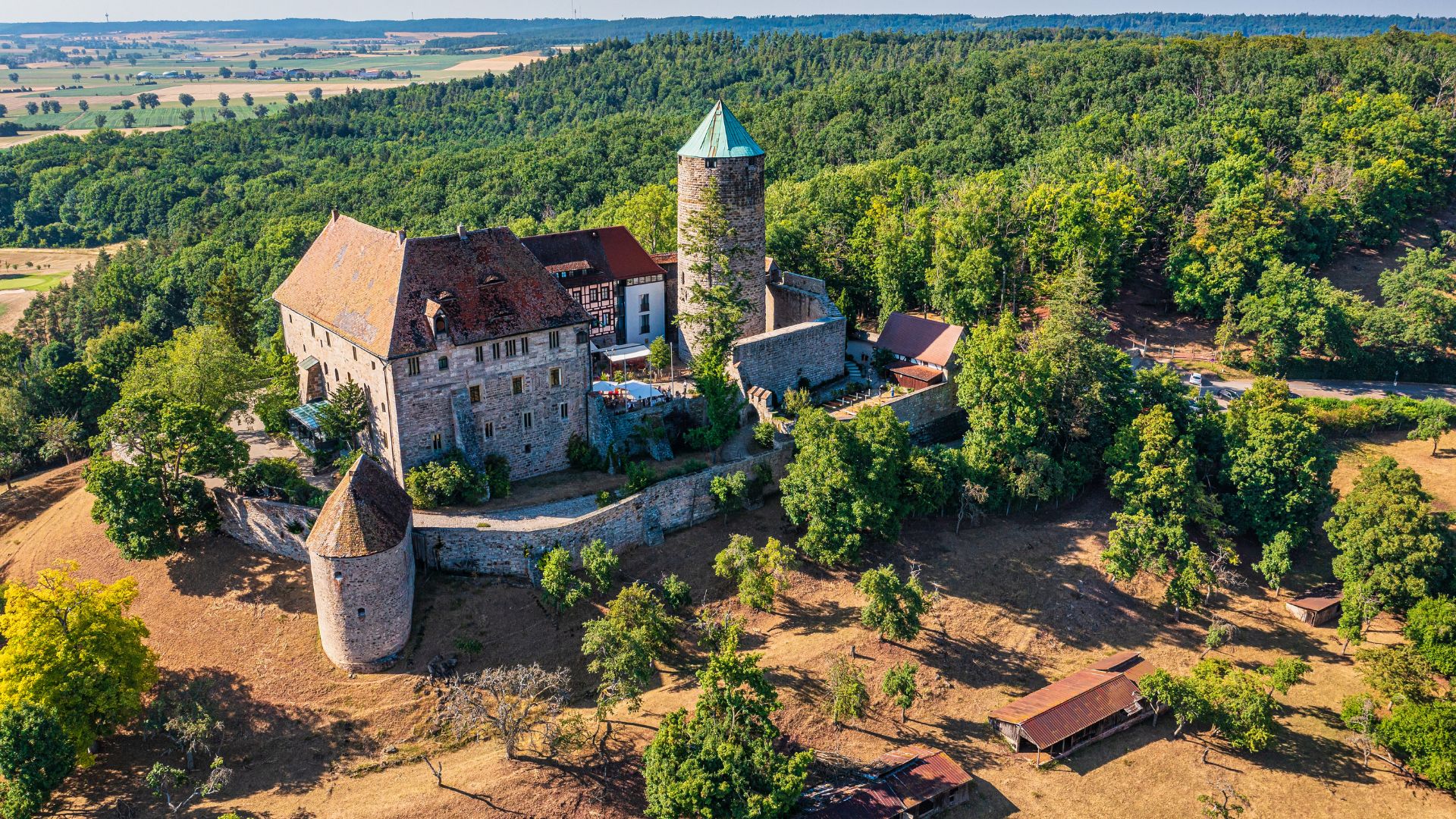 Burg Colmberg mit rundem Bergfried und umlaufender Mauer auf bewaldetem Hügel mit umliegender Landschaft